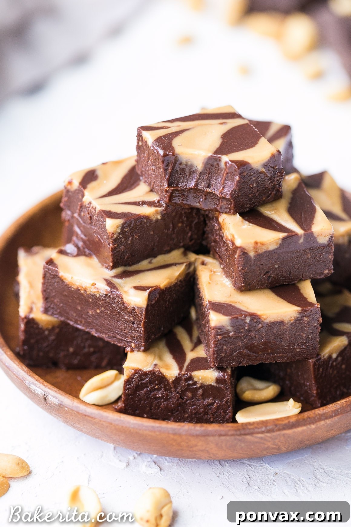 An inviting overhead shot of vegan chocolate peanut butter fudge squares, beautifully arranged on a wooden plate, with a delectable peanut butter swirl. One piece clearly shows a bite taken out, highlighting its creamy texture.