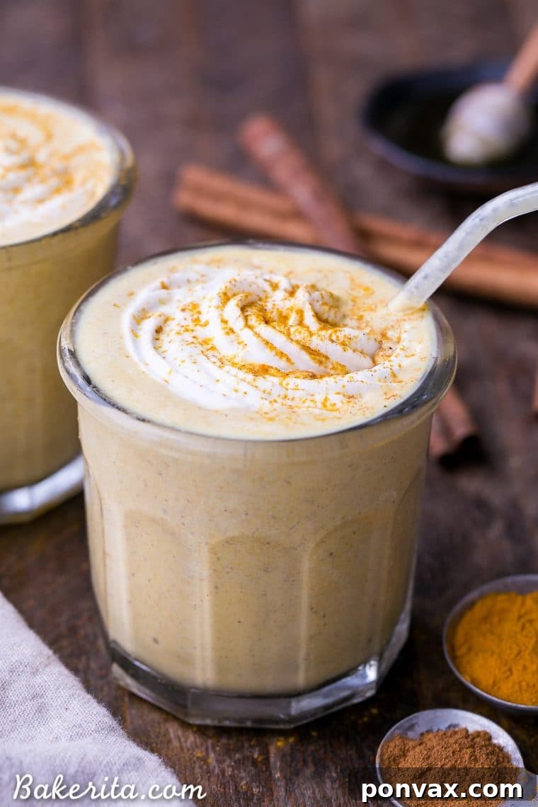 Side view of a glass of Golden Milkshake, showcasing its vibrant yellow color and creamy texture, topped with whipped cream and a sprinkle of spices.