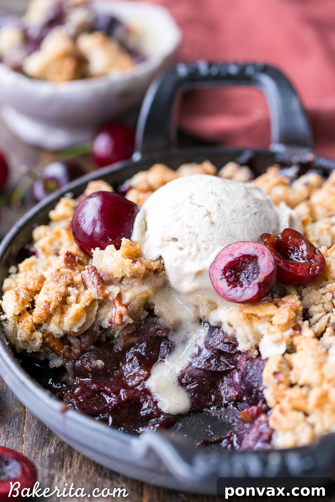 A top-down view of the grain-free cherry crisp in a rustic baking dish, with a spoon having scooped out a portion, highlighting the bubbling cherries and crunchy topping.