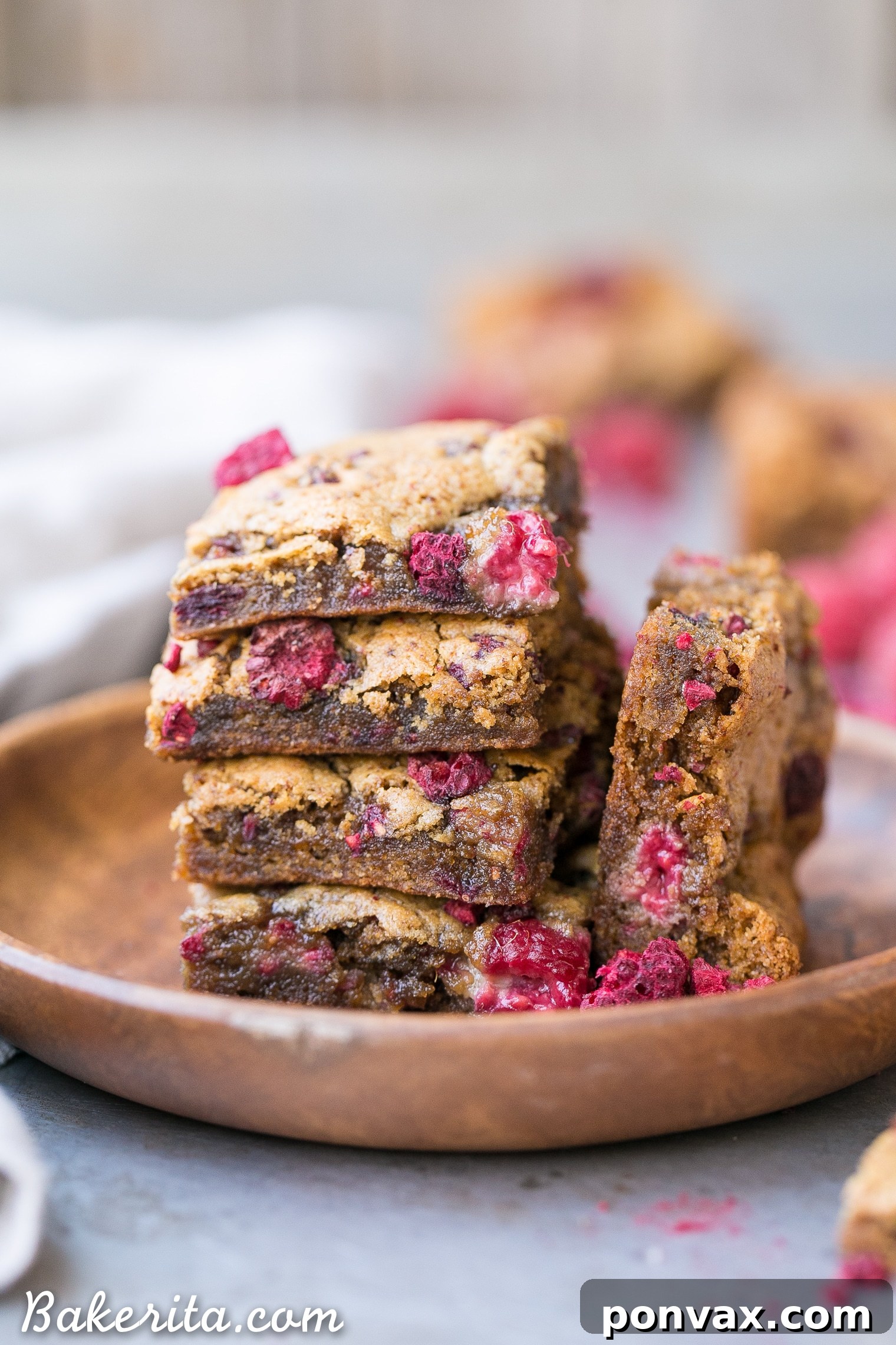 Close-up of a square of freshly baked vegan raspberry blondie on parchment paper, showing its moist, chewy texture and vibrant red raspberry pieces.