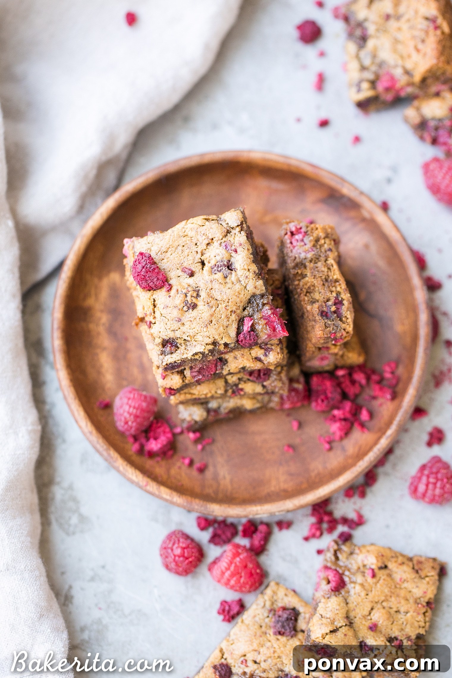 A close-up shot of a hand reaching for a piece of vegan raspberry blondie, emphasizing its appealing texture and fresh fruit.