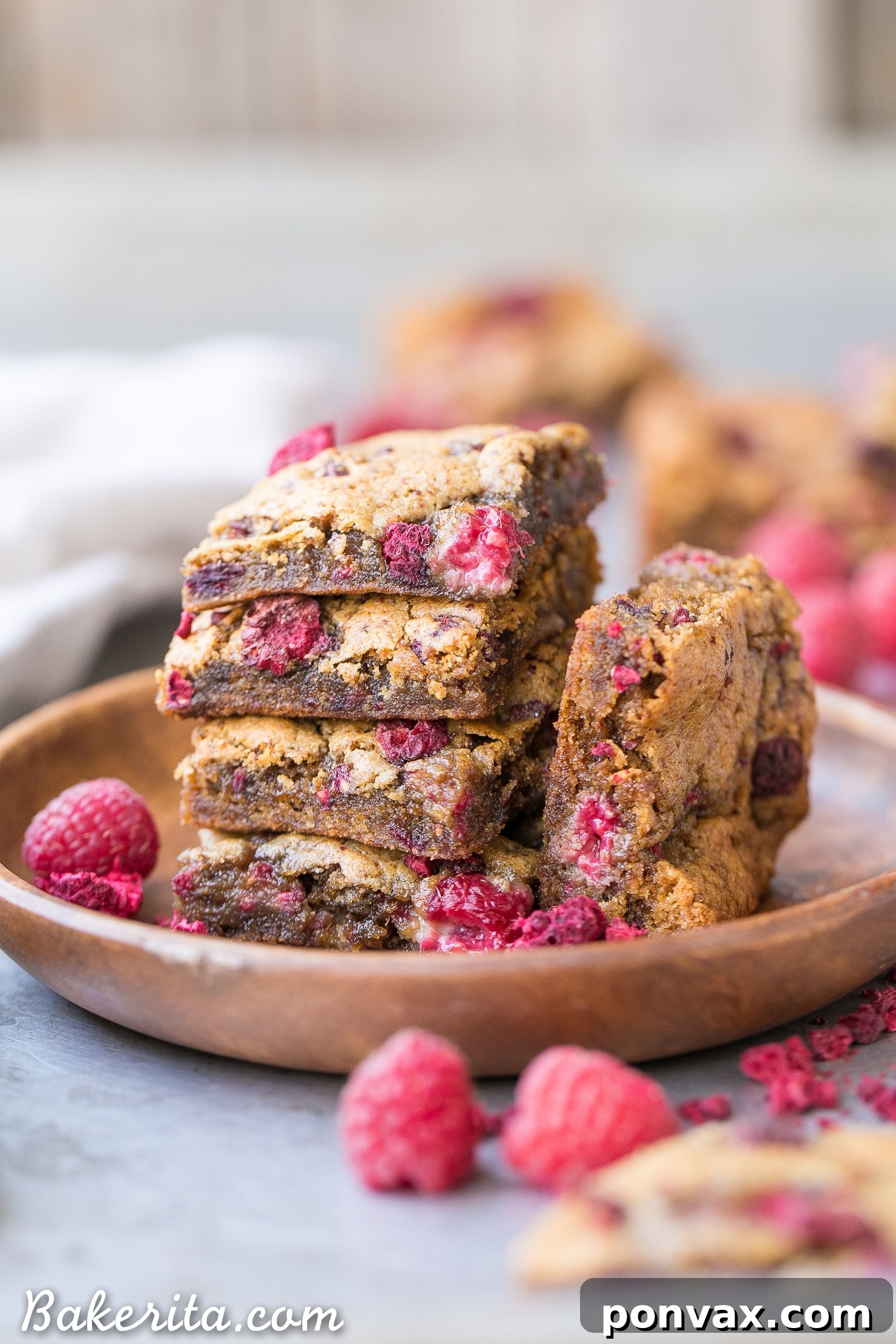 A stack of vegan raspberry blondies on a cooling rack, perfectly golden brown and speckled with raspberries.