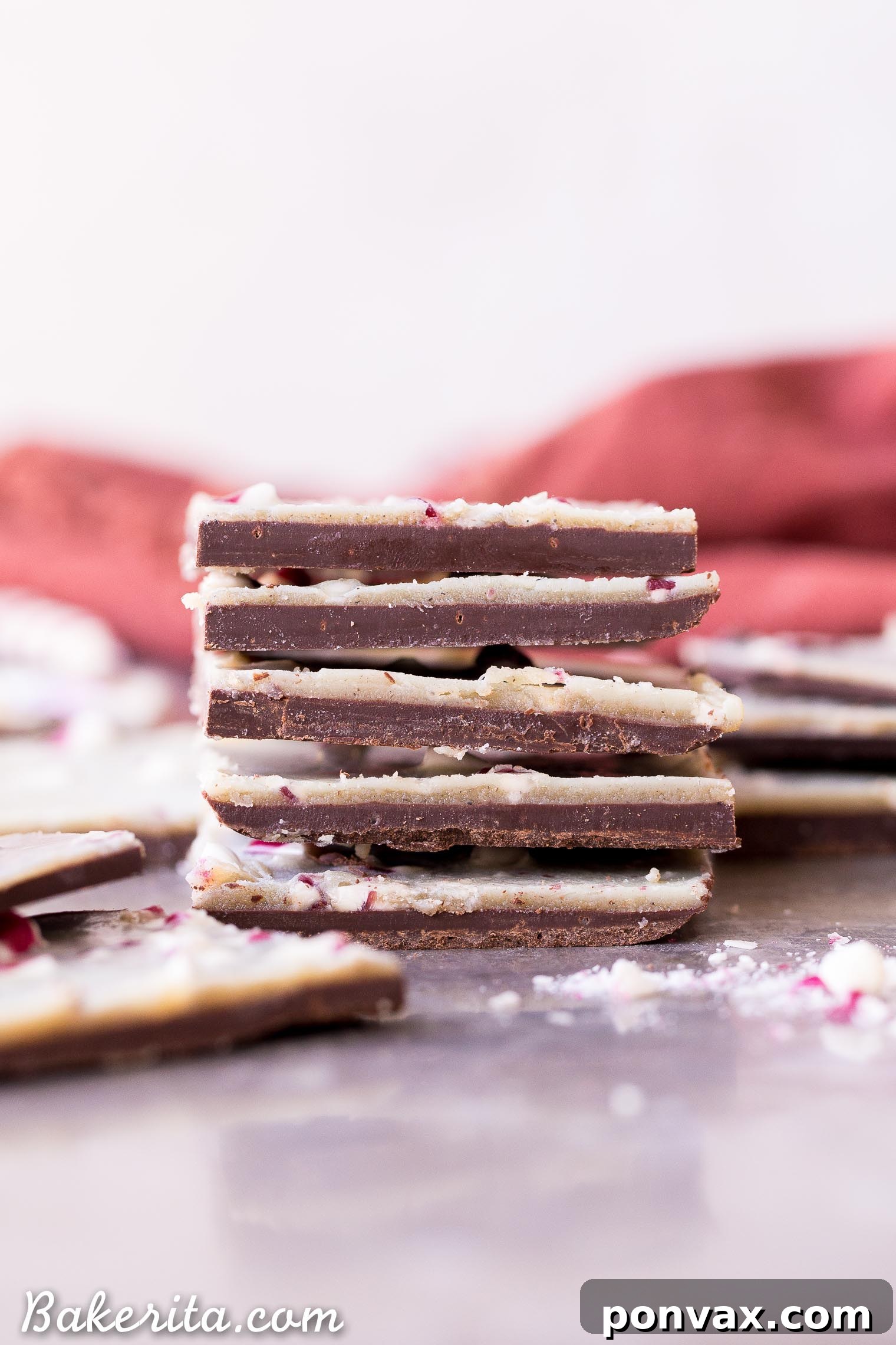 Close-up of freshly prepared Vegan Chocolate Peppermint Bark on parchment paper, ready to be chilled. The contrasting dark and homemade vegan white chocolate layers are visible, topped generously with crushed peppermint candies for a festive crunch.