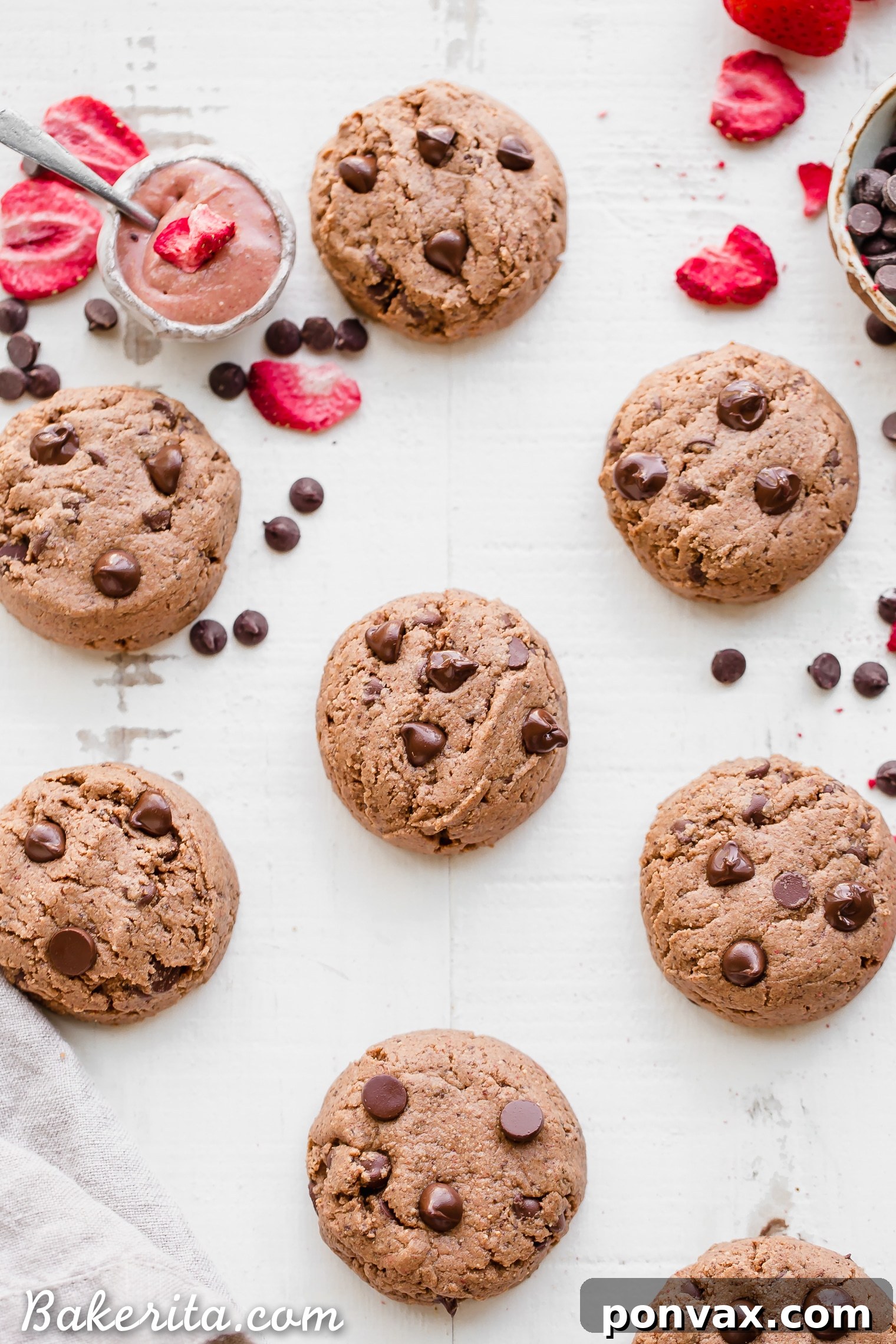 A batch of freshly baked Flourless Strawberry Chocolate Chip Cookies cooling on a rack, showing their vibrant pink hue and melted chocolate.