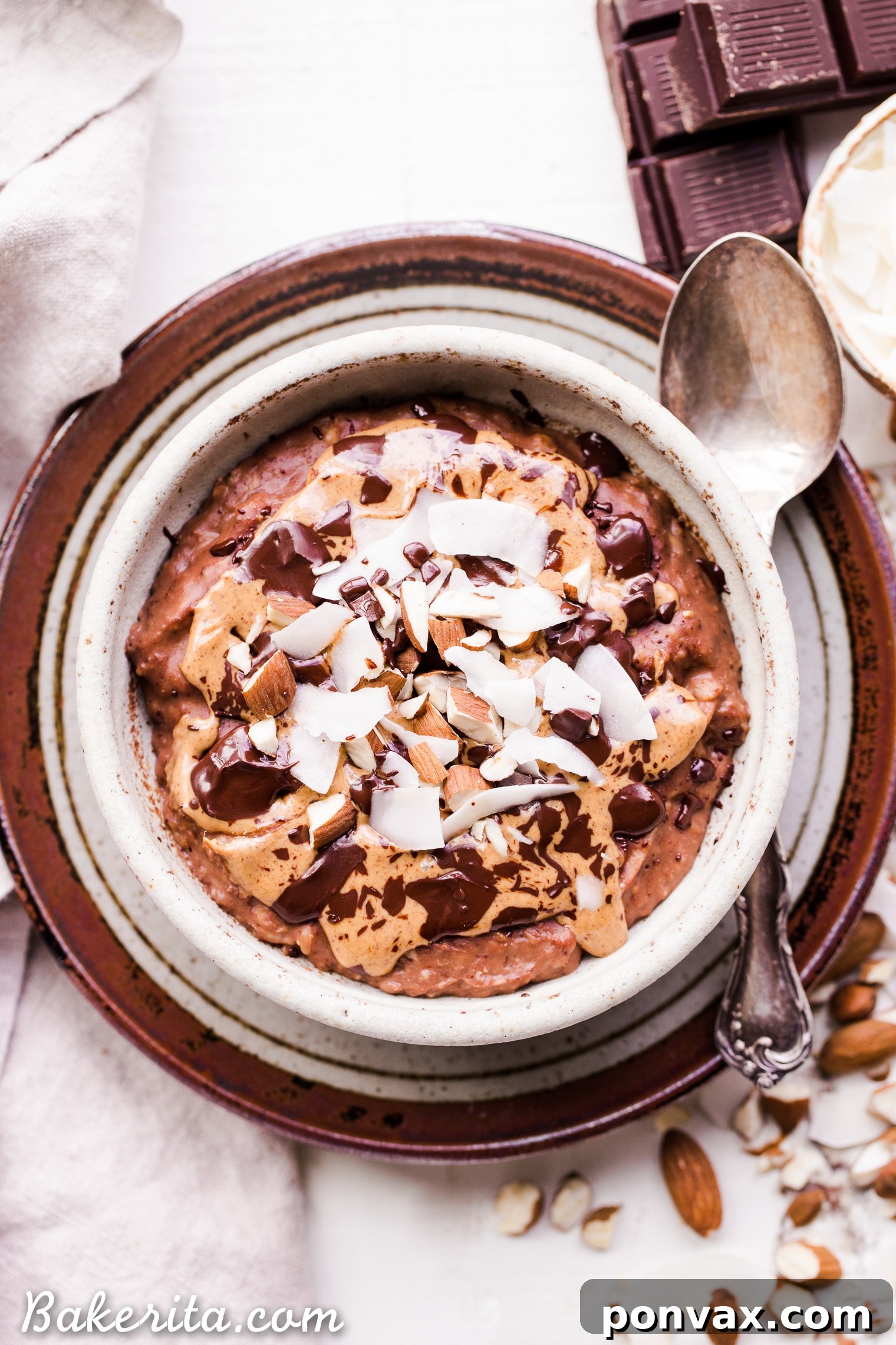 Overhead view of a prepared bowl of Almond Joy Oatmeal, richly topped with shredded coconut, crunchy almond pieces, and a generous dollop of almond butter.