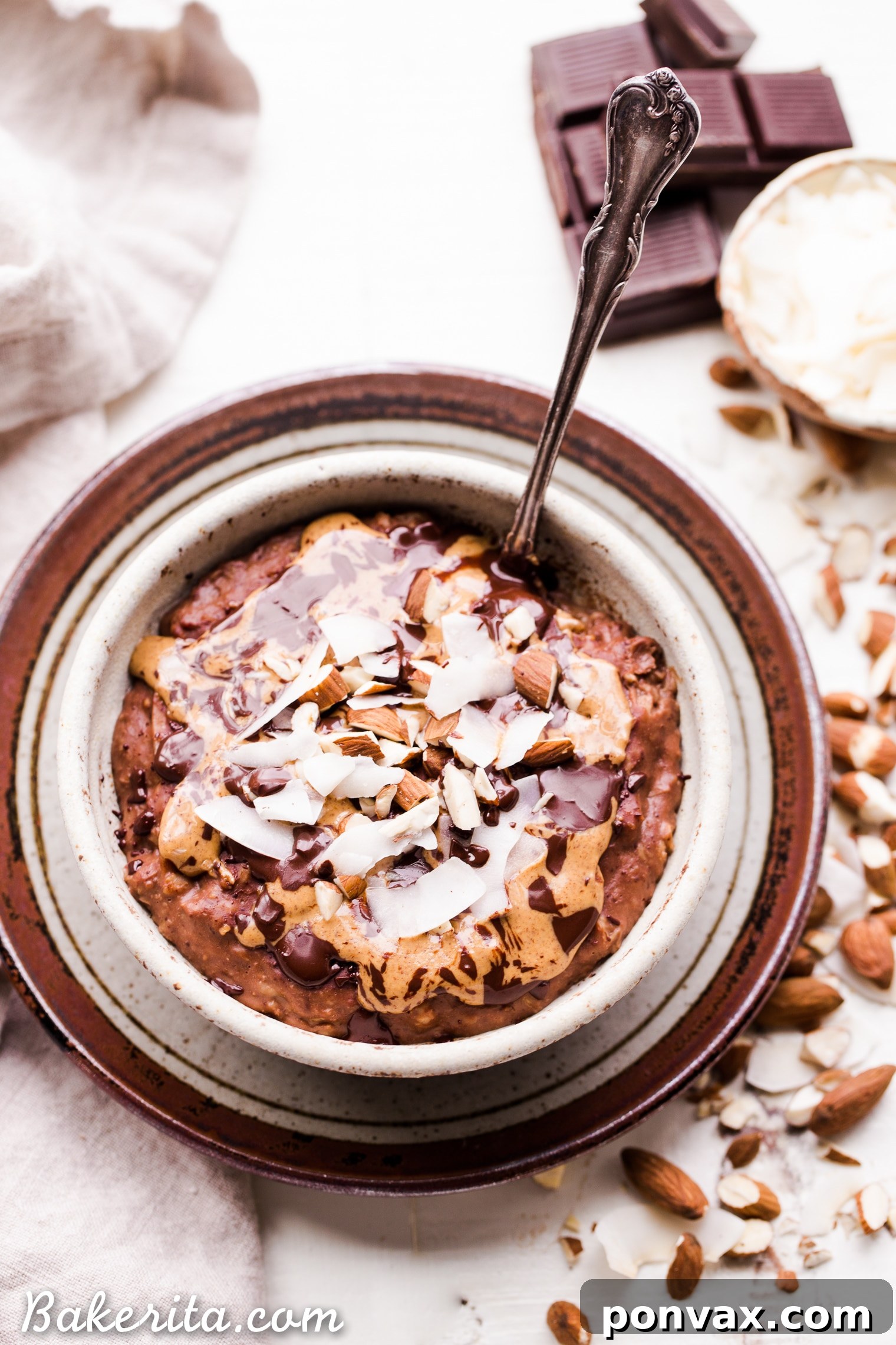 A bowl of Almond Joy Oatmeal, garnished with a generous amount of toasted coconut, crushed almonds, and a drizzle of melted dark chocolate, presented on a rustic wooden surface.