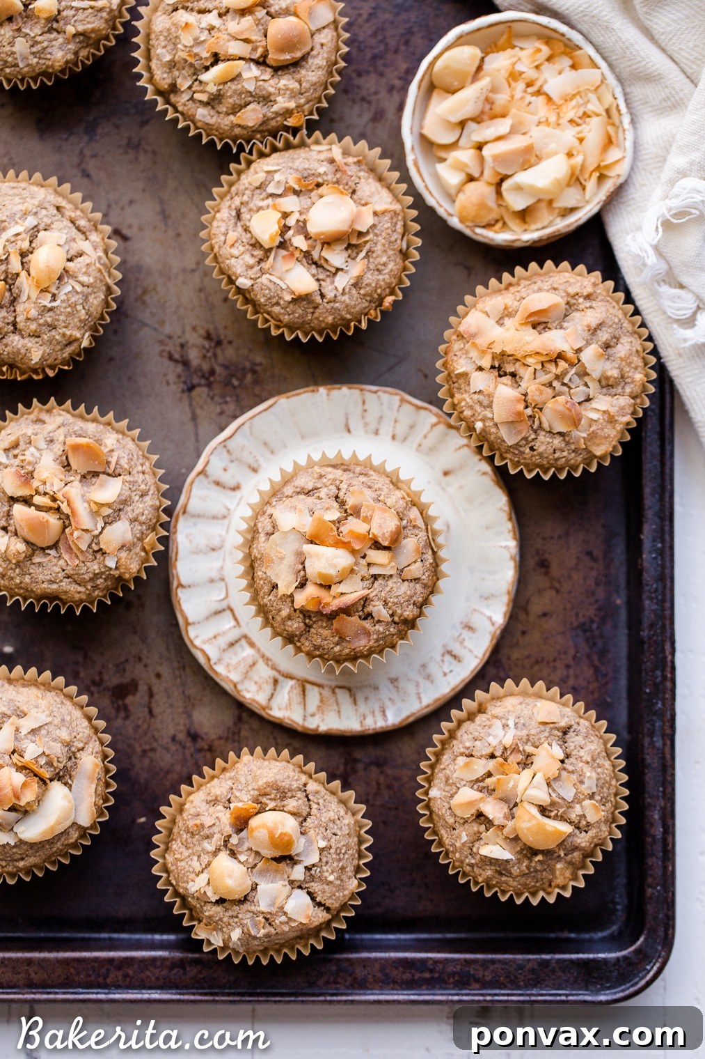 Wholesome Macadamia Nut Coconut Banana Muffins Vegan Gluten Free 6 An overhead shot of Macadamia Nut Coconut Banana Muffins, some whole, some with a bite taken out, resting on a white platter. The generous amount of nuts and coconut are clearly visible on their textured surfaces, inviting a delicious tasting.