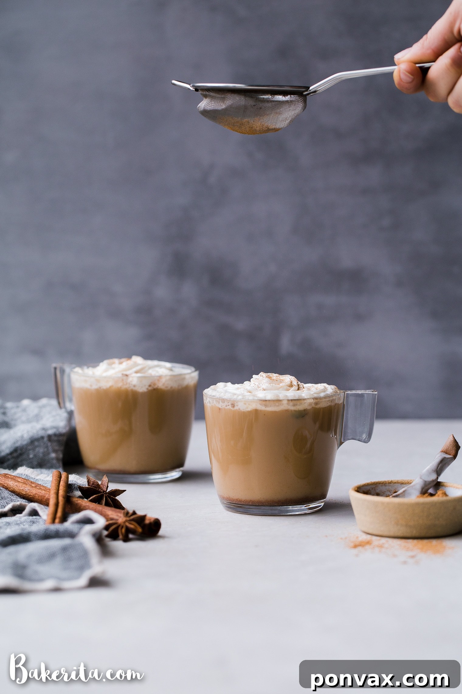 A freshly brewed, frothy Vegan Chai Latte in a tall glass mug, topped with a delicate design made from a sprinkle of chai spices, on a light background.