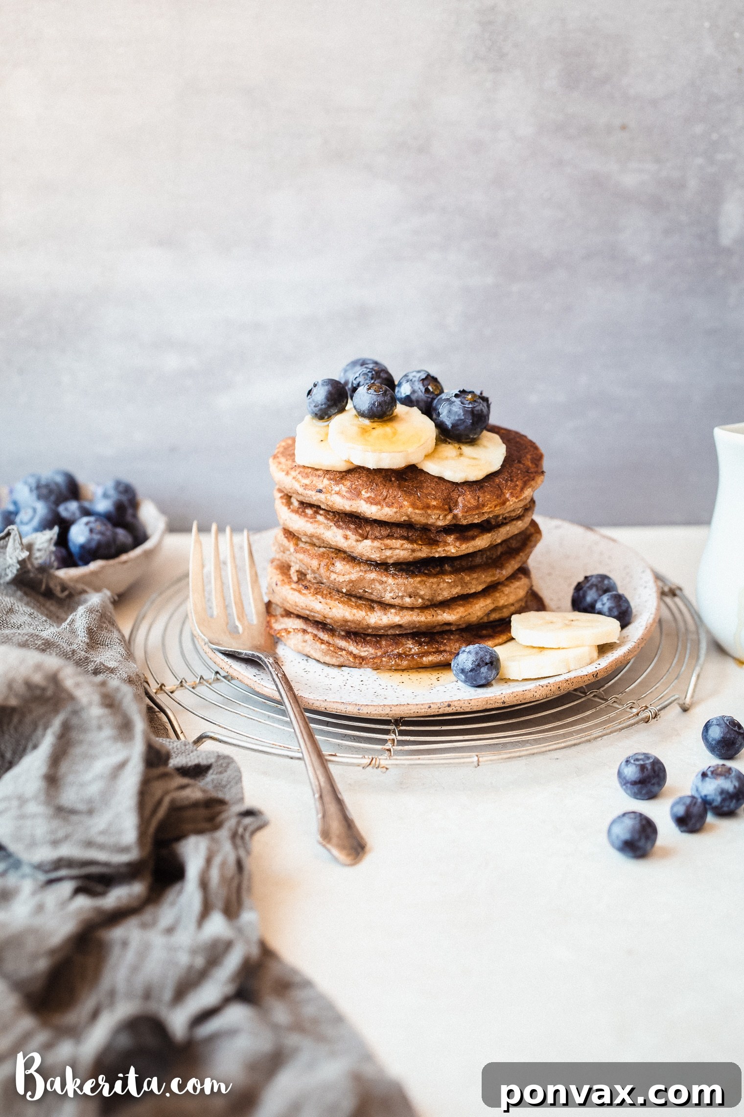 A beautiful stack of perfectly cooked gluten-free vegan banana blueberry pancakes topped with fresh fruit and a generous drizzle of maple syrup.