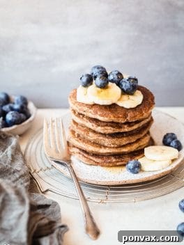 Delicious stack of Banana Blueberry Pancakes topped with coconut cream, blueberries, and maple syrup.