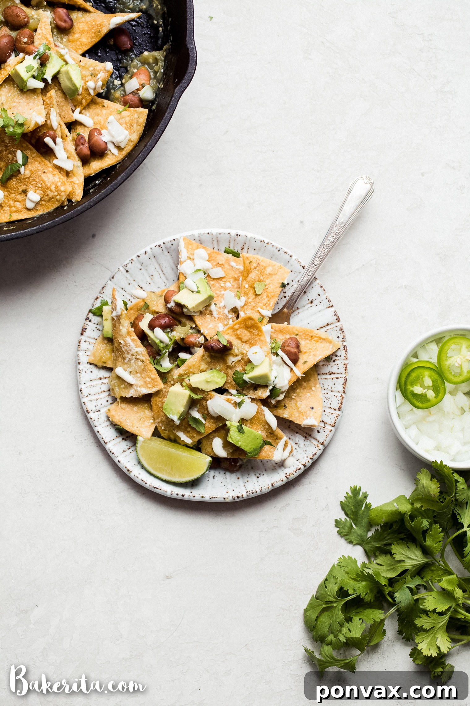 A wide shot of two servings of Vegan Chilaquiles Verdes, generously topped with avocado, cilantro, and vegan sour cream, on a wooden table.