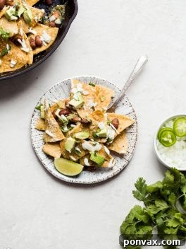 A bowl of Vegan Chilaquiles Verdes, showcasing the green salsa, baked chips, and creamy toppings, served with a fork.