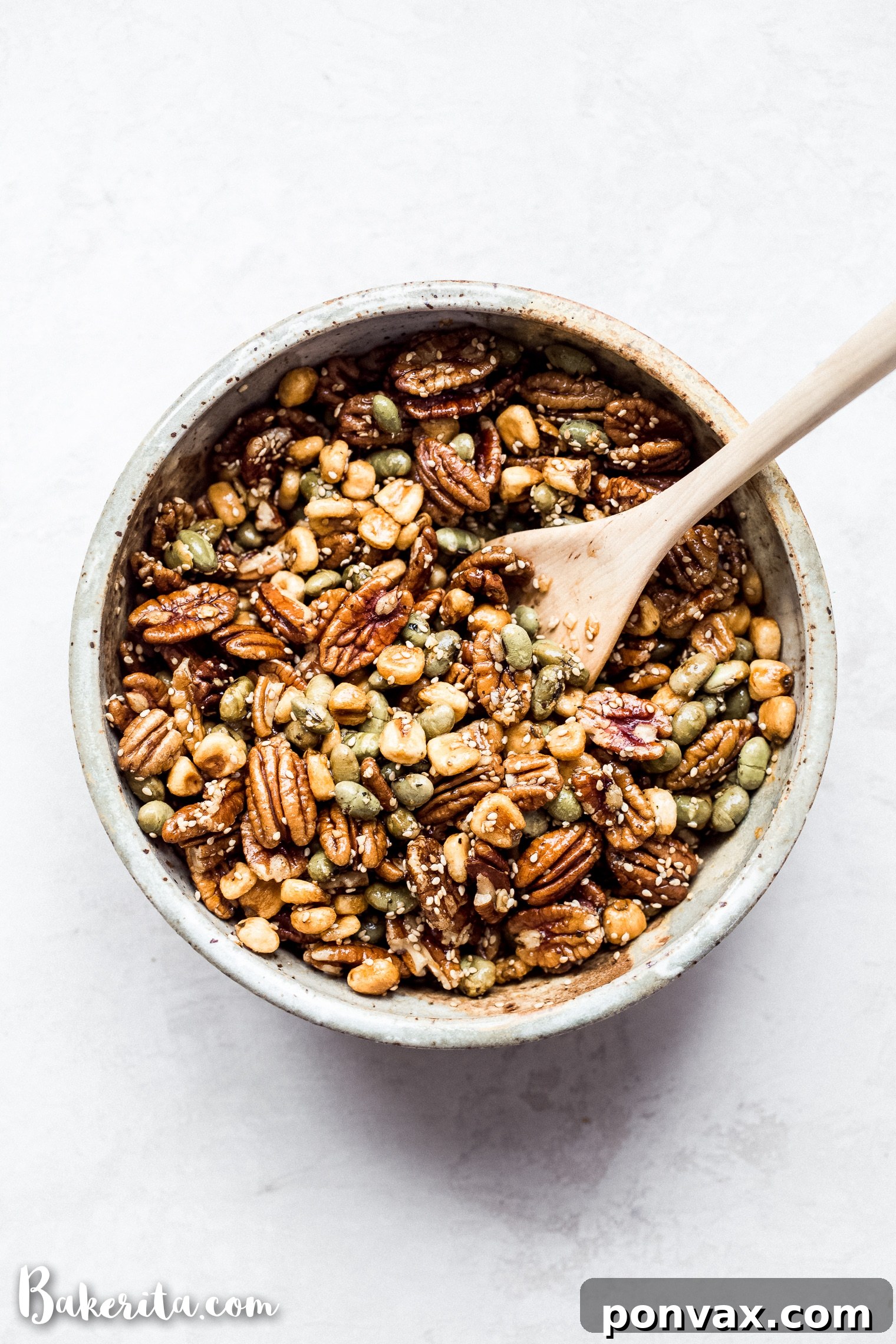 A hand reaches into a generous pile of Sesame Tamari Pecan Snack Mix, highlighting its alluring texture and inviting appearance.