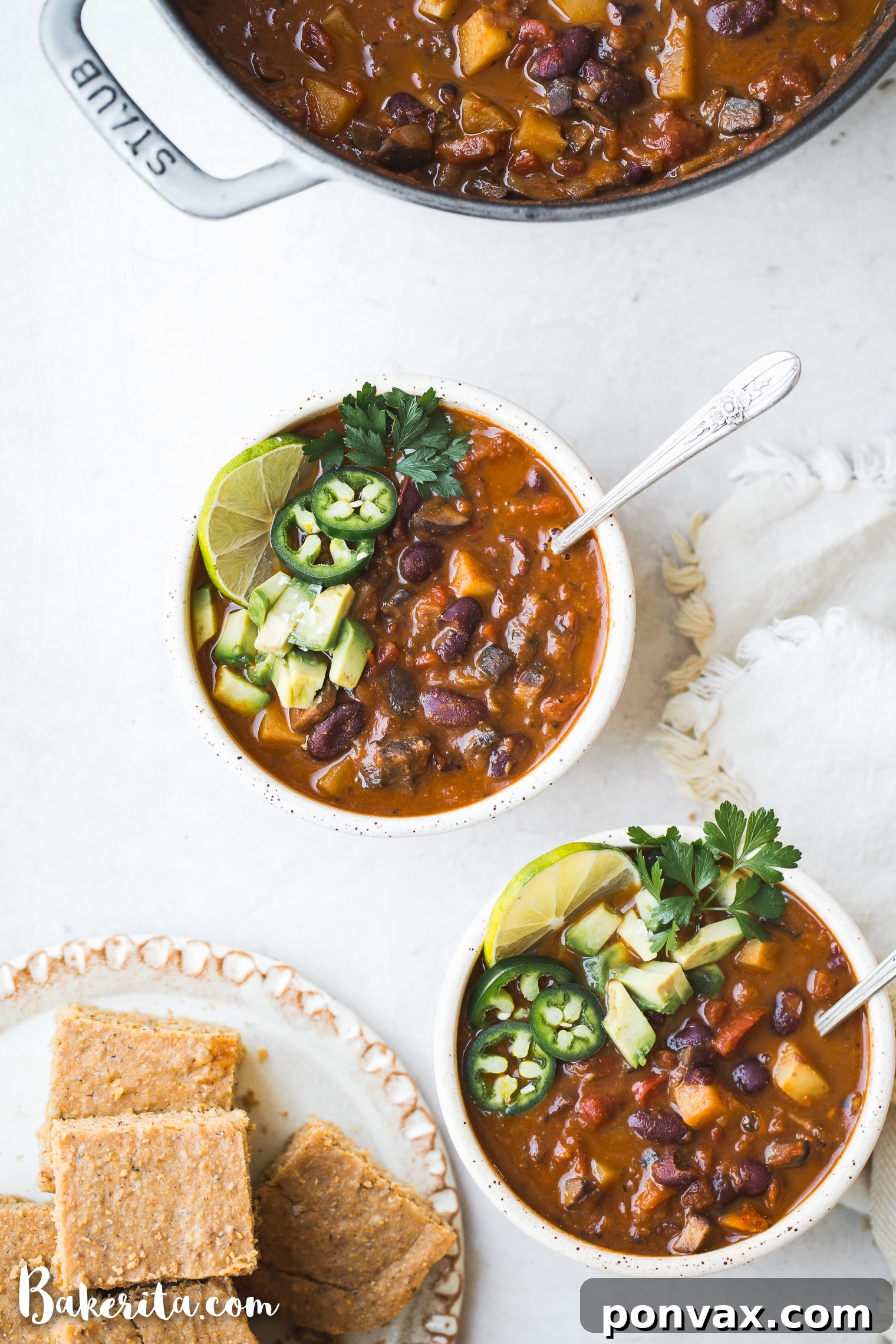 A close-up shot of vegan chili in a bowl, topped with diced avocado, green onions, and a sprinkle of fresh cilantro.