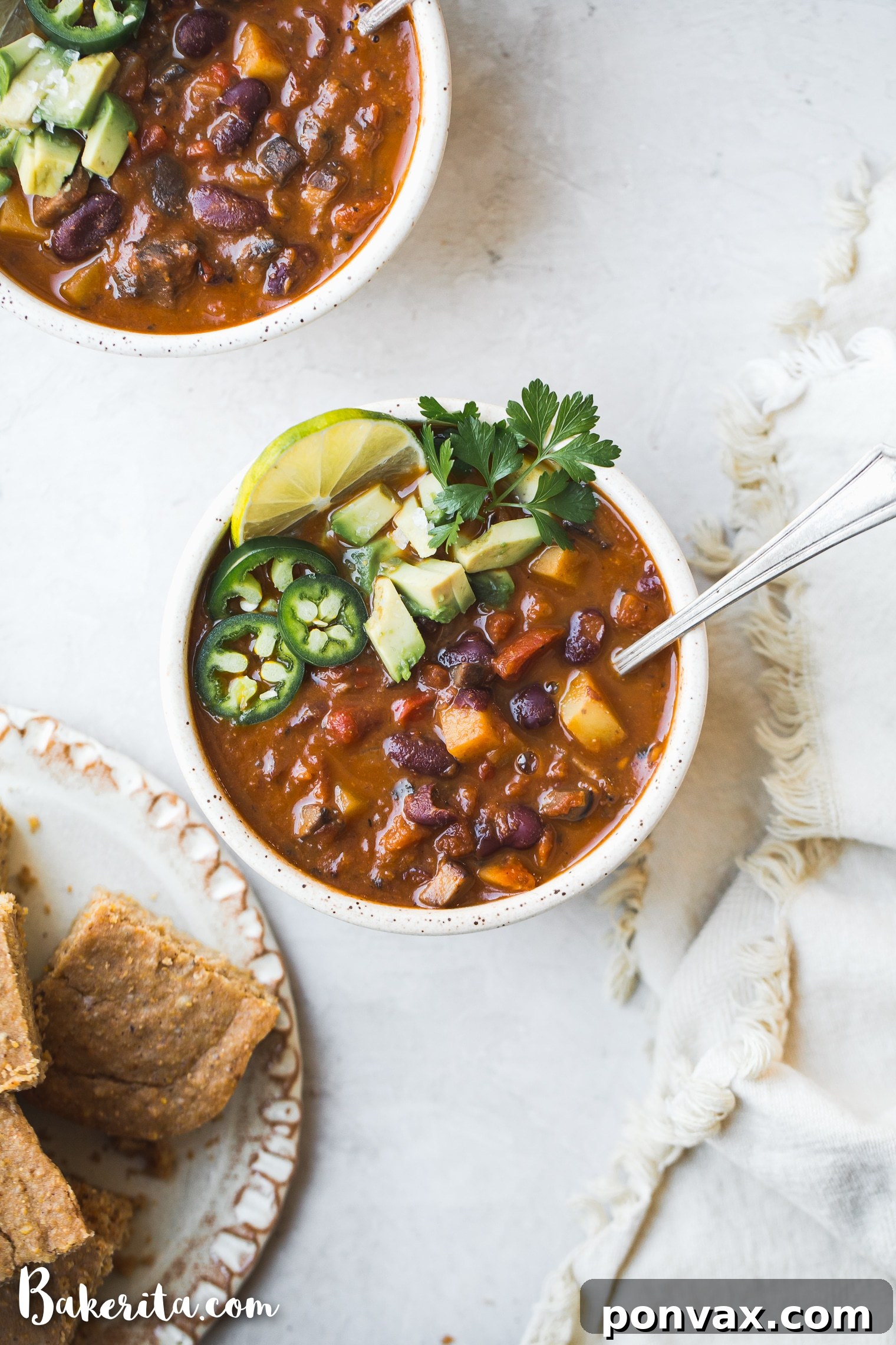 A rustic bowl of vegan chili, served with a side of gluten-free vegan cornbread on a wooden board.