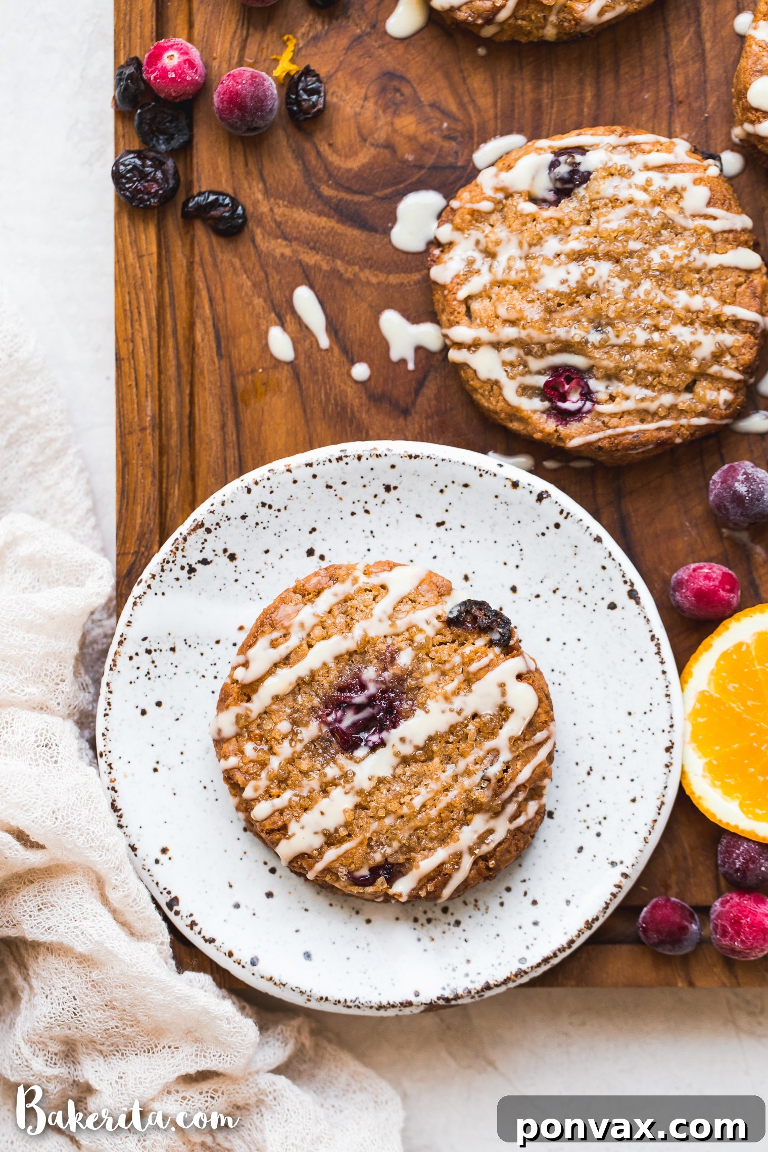 A close-up view of two finished gluten-free vegan cranberry orange scones on a white ceramic plate, highlighting their vibrant color and glaze.