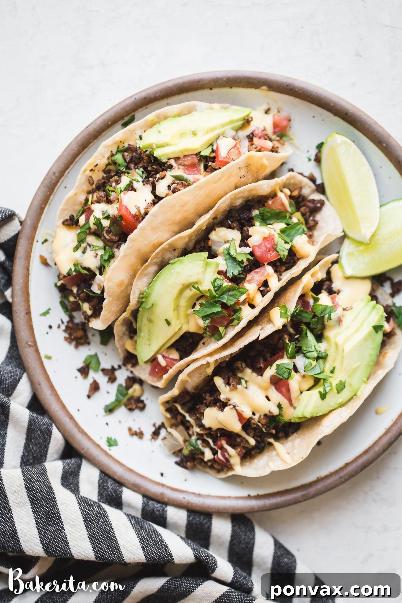 Vegan taco meat served in corn tortillas with vegan cheese sauce, fresh pico de gallo, slices of ripe avocado, and lime wedges, beautifully arranged on a ceramic plate.