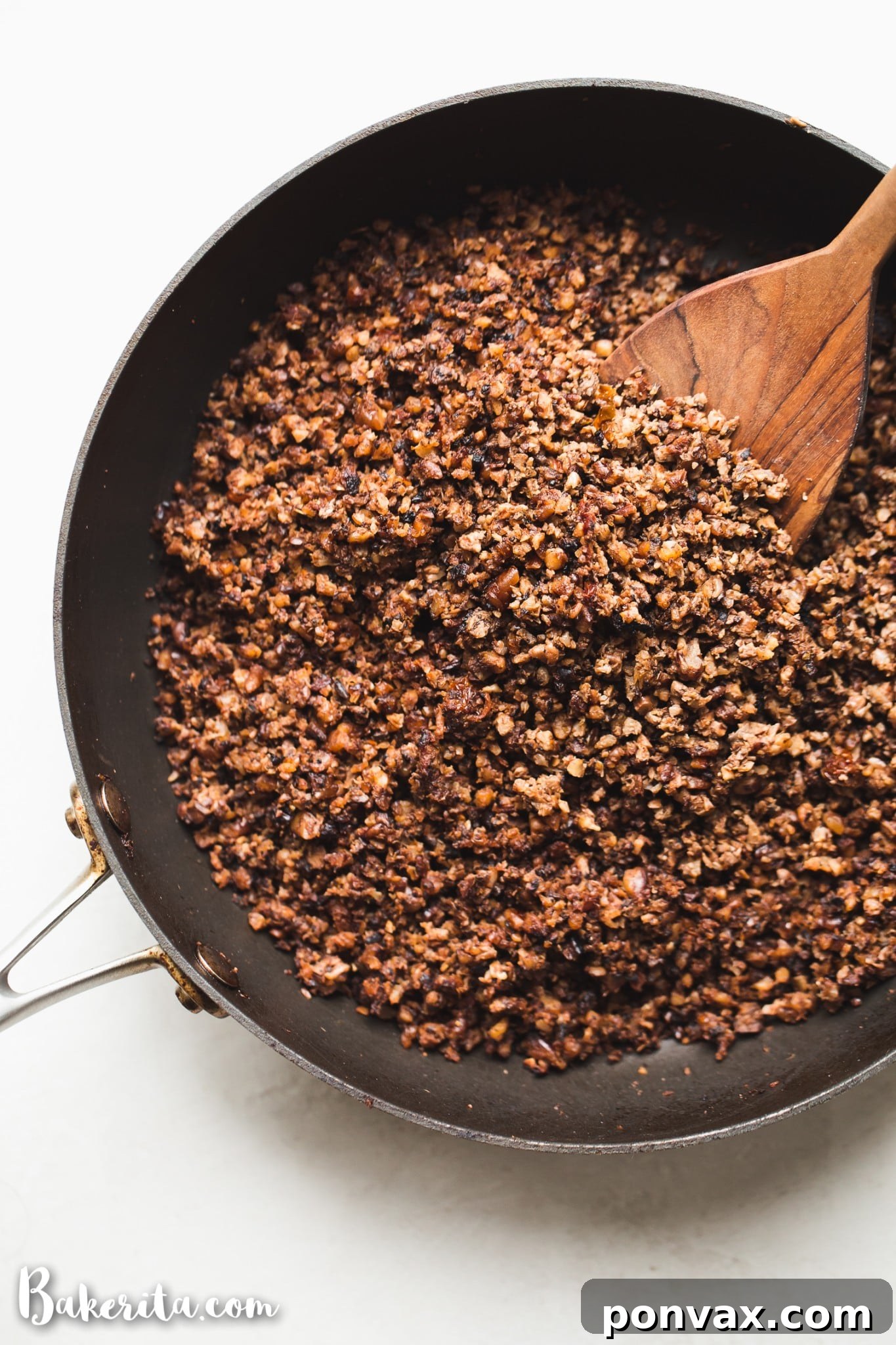 A close-up view of flavorful vegan taco meat simmering in a black cast iron pan, with a wooden spoon resting nearby, inviting viewers to imagine its rich texture and aroma.