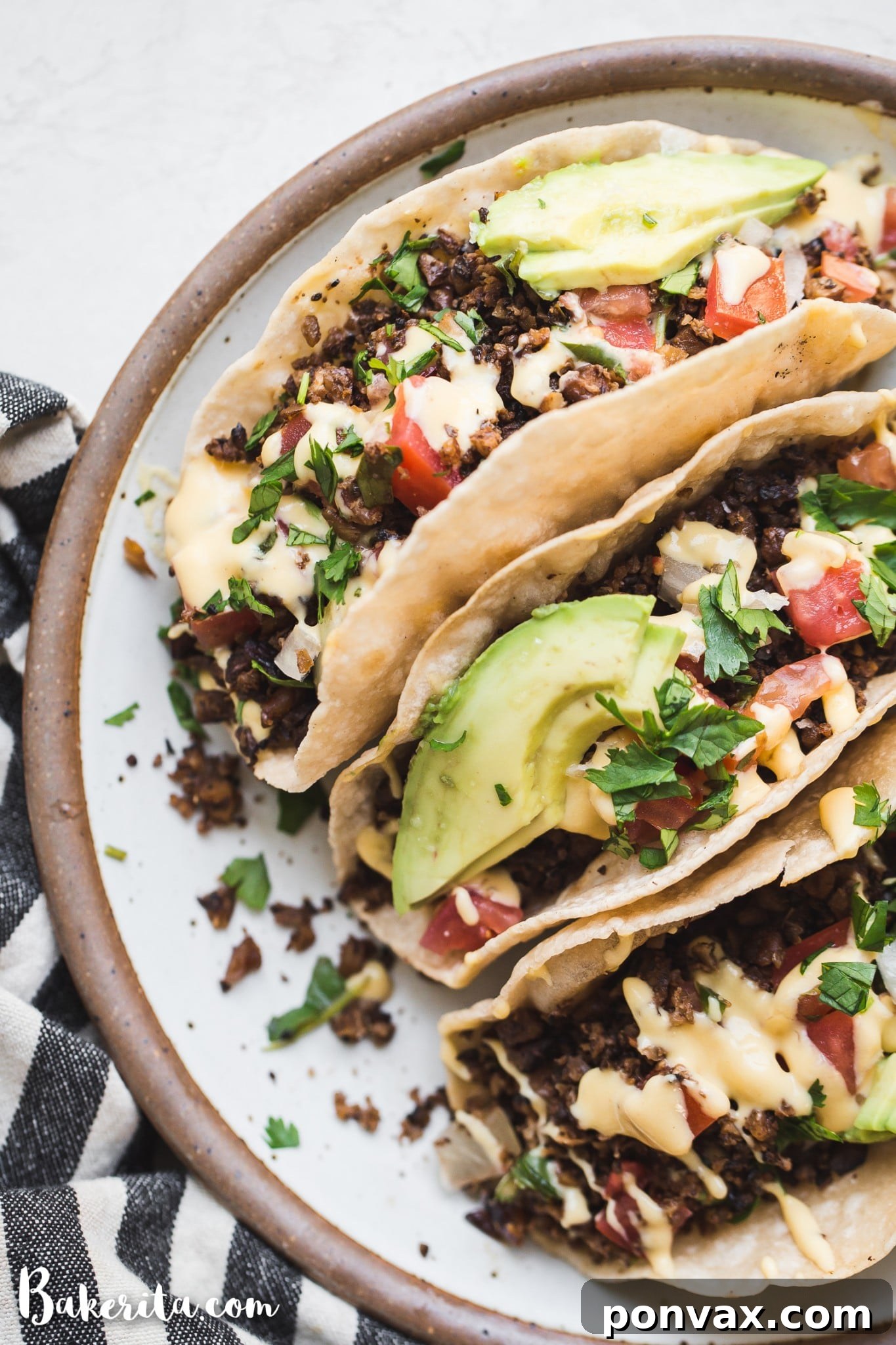 Three beautifully assembled tacos on a plate, generously filled with savory vegan ground taco meat, drizzled with a rich vegan cheese sauce, topped with fresh avocado slices, vibrant pico de gallo, and a sprinkle of fresh cilantro.