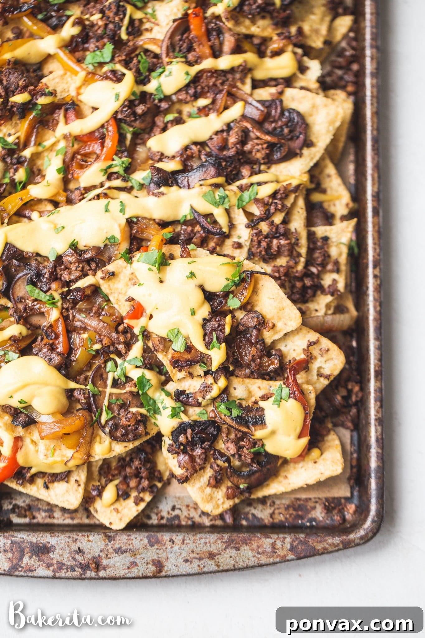 Close-up shot of vegan nachos showing layers of seasoned chips, vegan cheese sauce, and various fresh toppings, emphasizing the rich texture and vibrant colors.