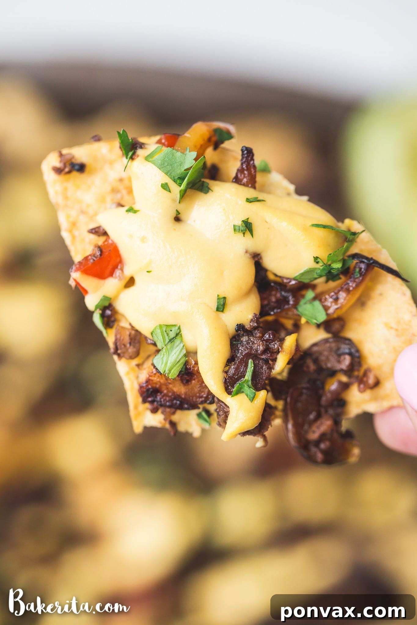 A close-up of a hand reaching for a loaded vegan nacho, showcasing the vibrant and fresh ingredients atop crispy tortilla chips.