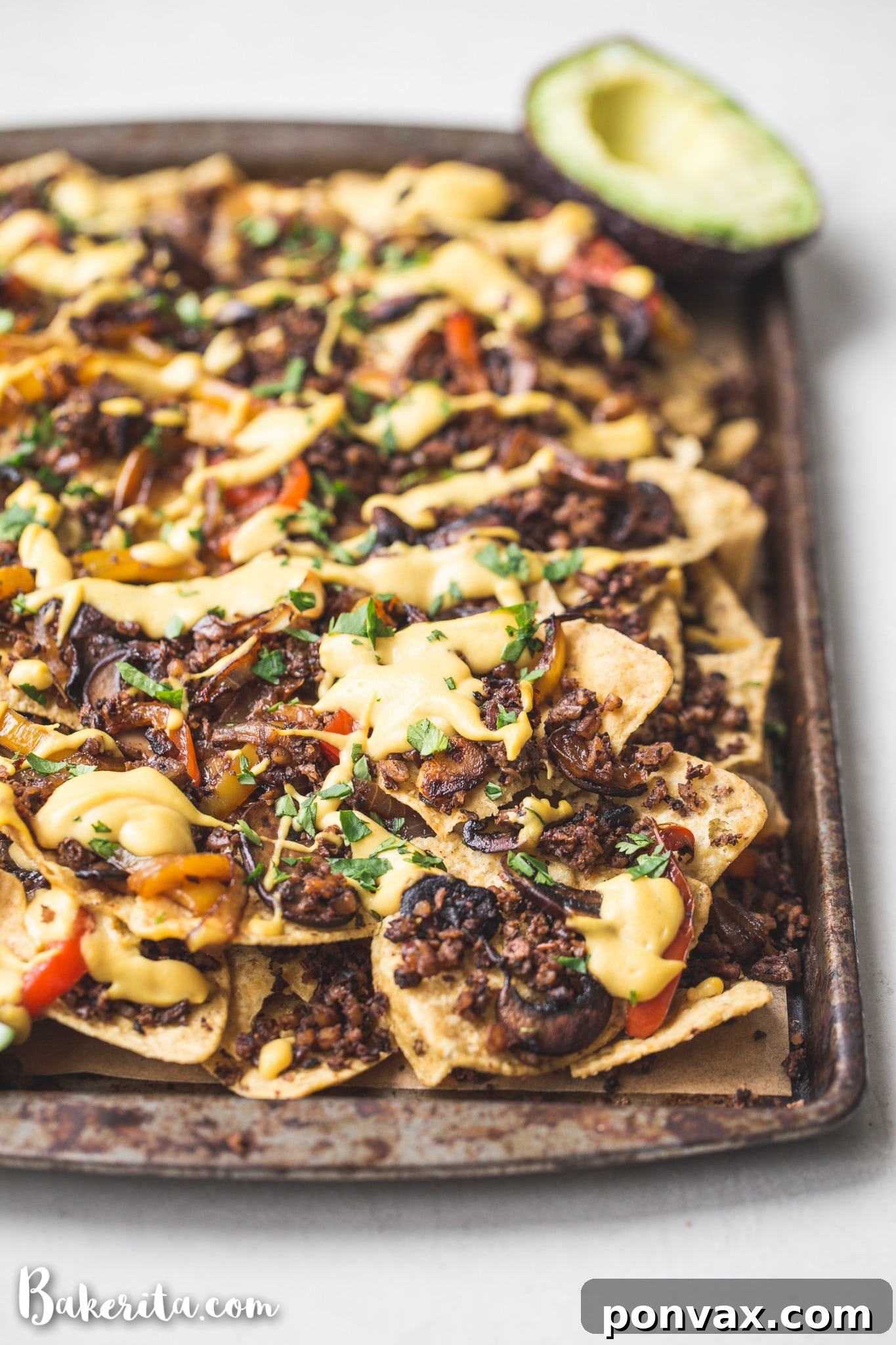 A close-up overhead shot of a pan of finished vegan nachos, showcasing the various layers of toppings, cheese sauce, and fresh cilantro, ready to be served.