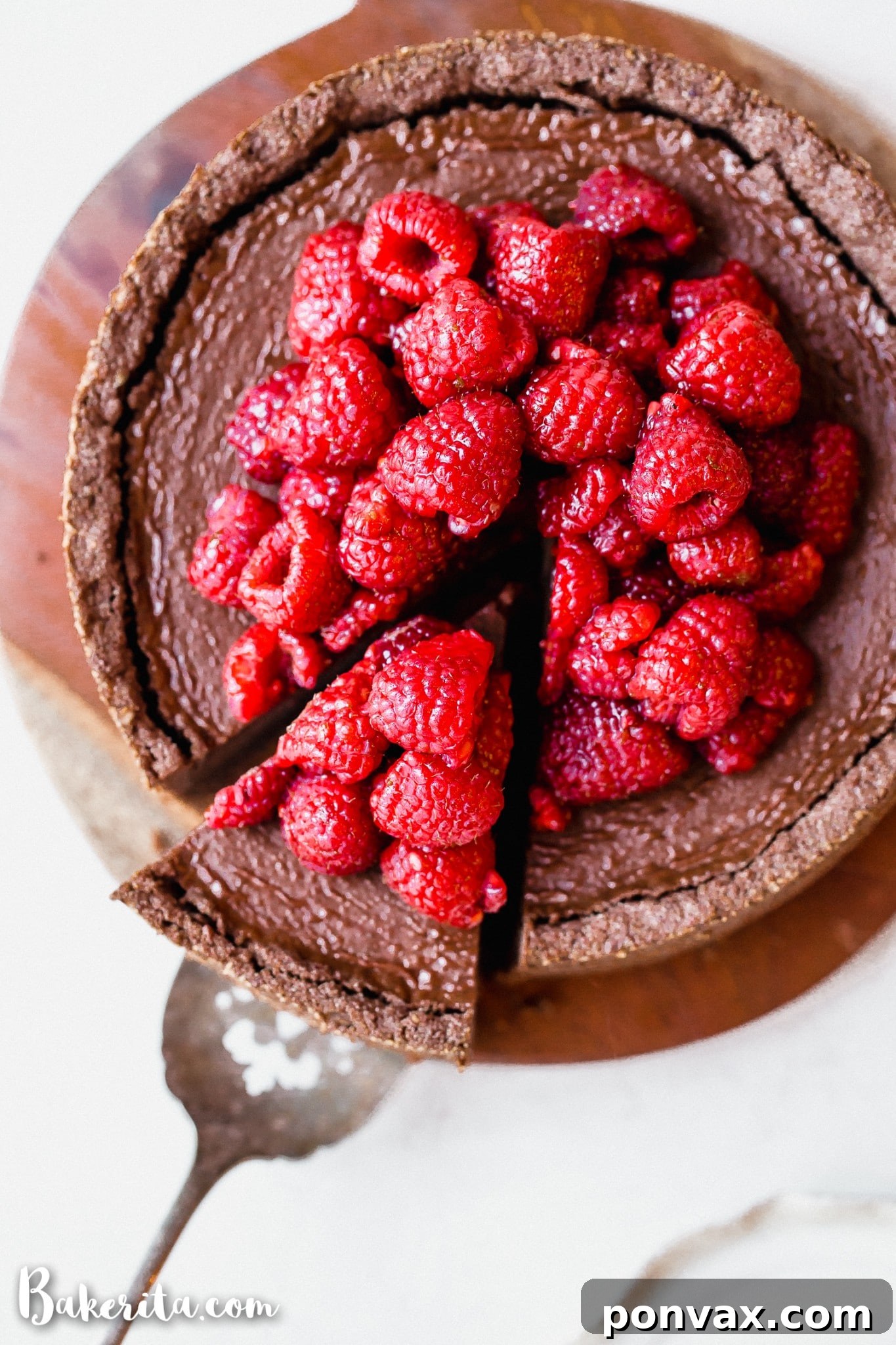 A beautifully sliced Baked Vegan Chocolate Cheesecake, garnished with fresh raspberries and a sprinkle of cacao powder.