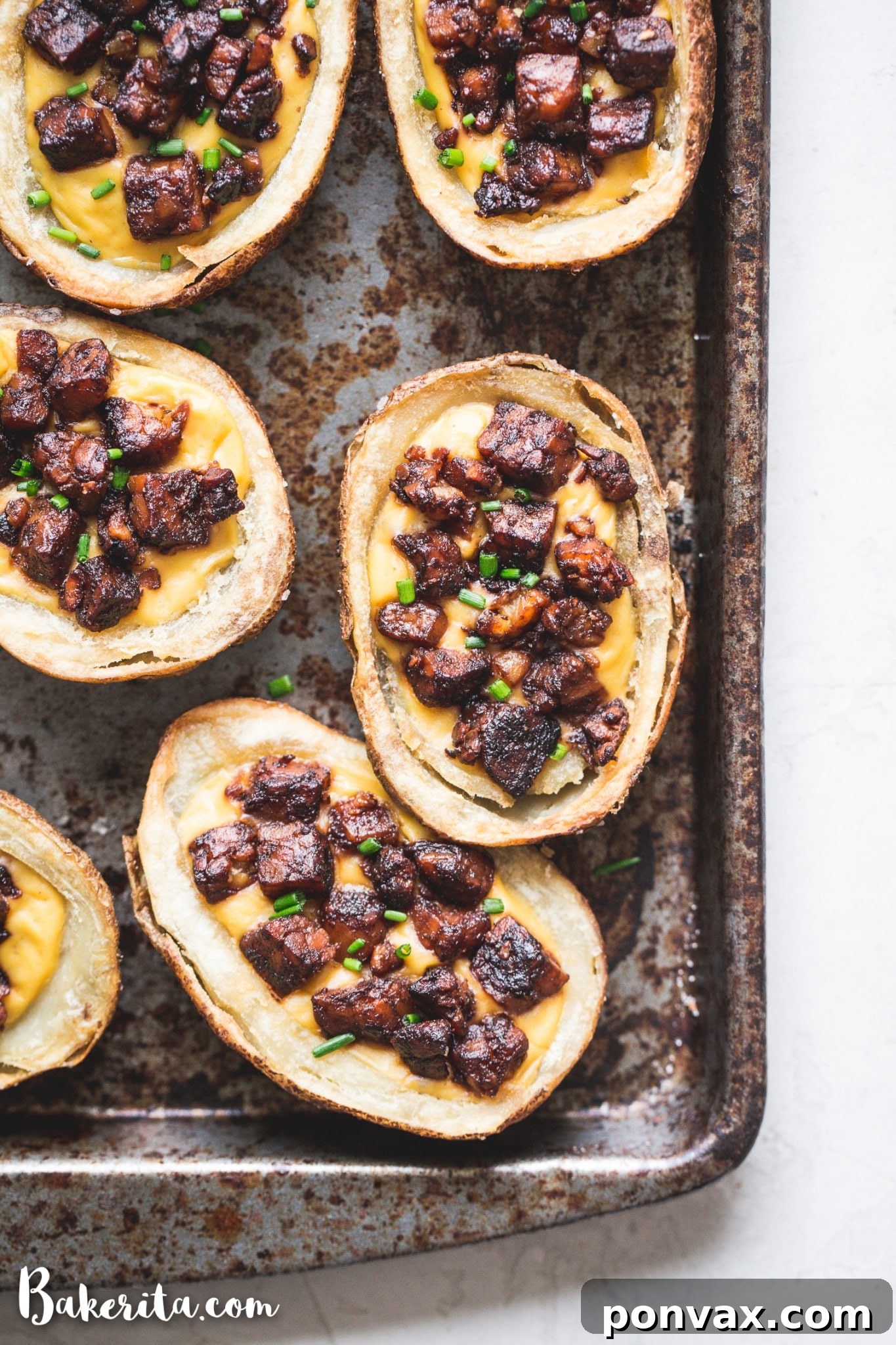 Delicious baked vegan potato skins with vegan cheese sauce and tempeh bacon bits, garnished with chives.
