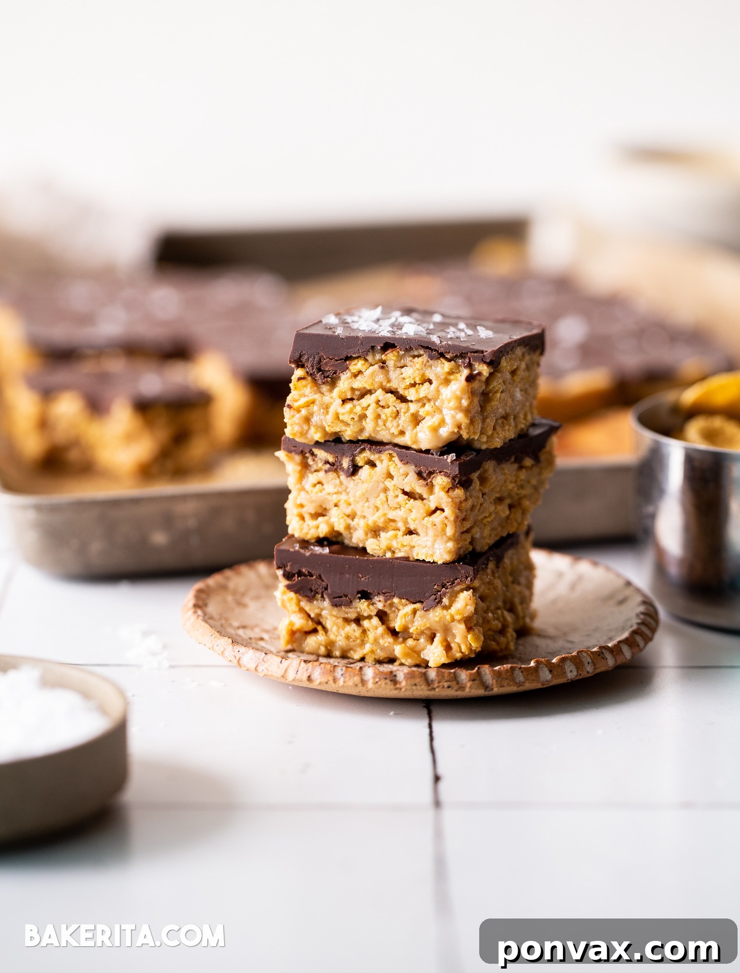 A hand holding a perfectly cut square of peanut butter cornflake bar, highlighting the layers and crunchy texture.