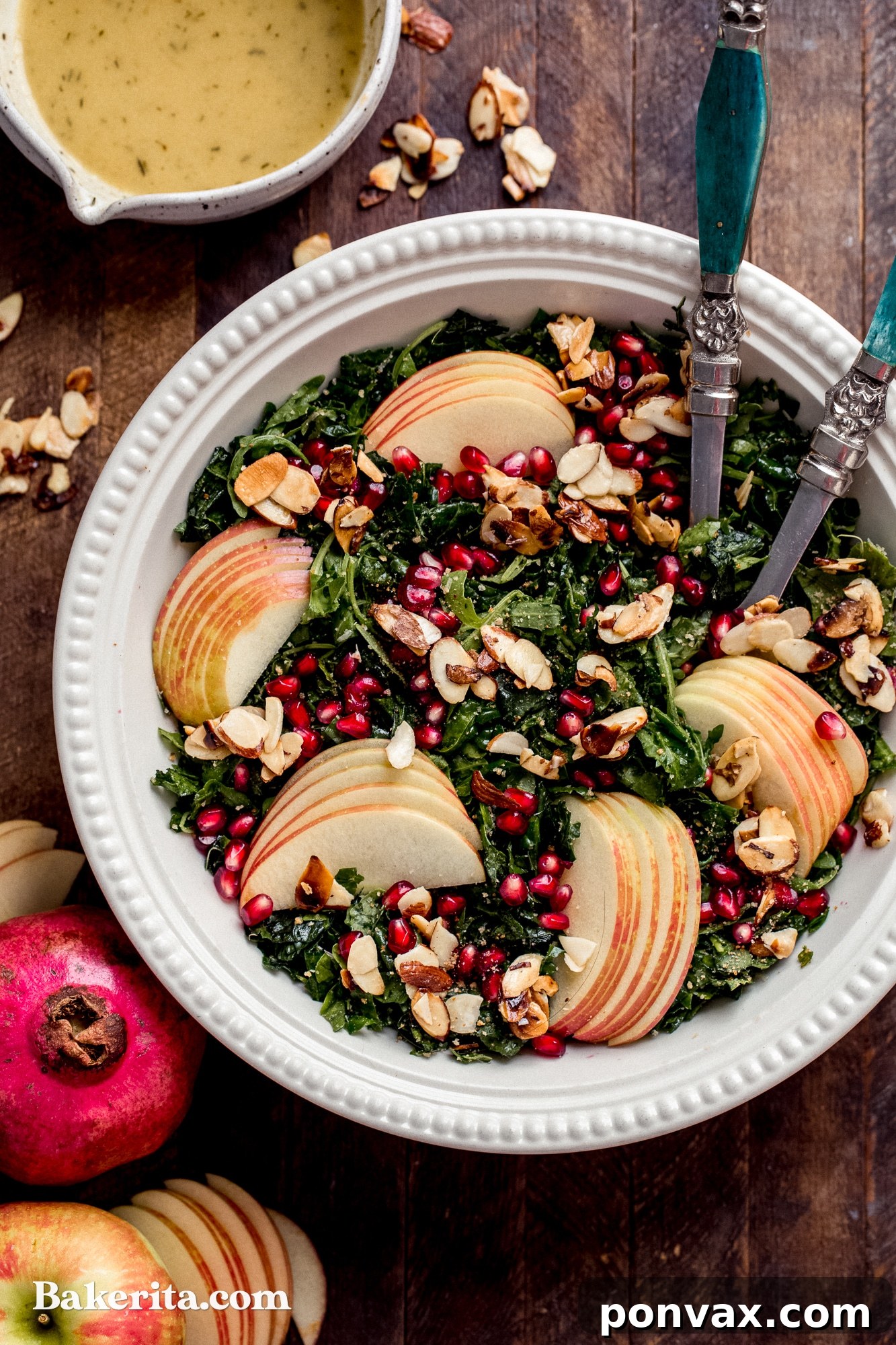 A vibrant close-up of Autumn Kale Harvest Salad featuring thinly sliced kale, bright red pomegranate seeds, golden Honeycrisp apple slices, and crunchy candied almonds, tossed in a shimmering Apple Cider Vinaigrette.