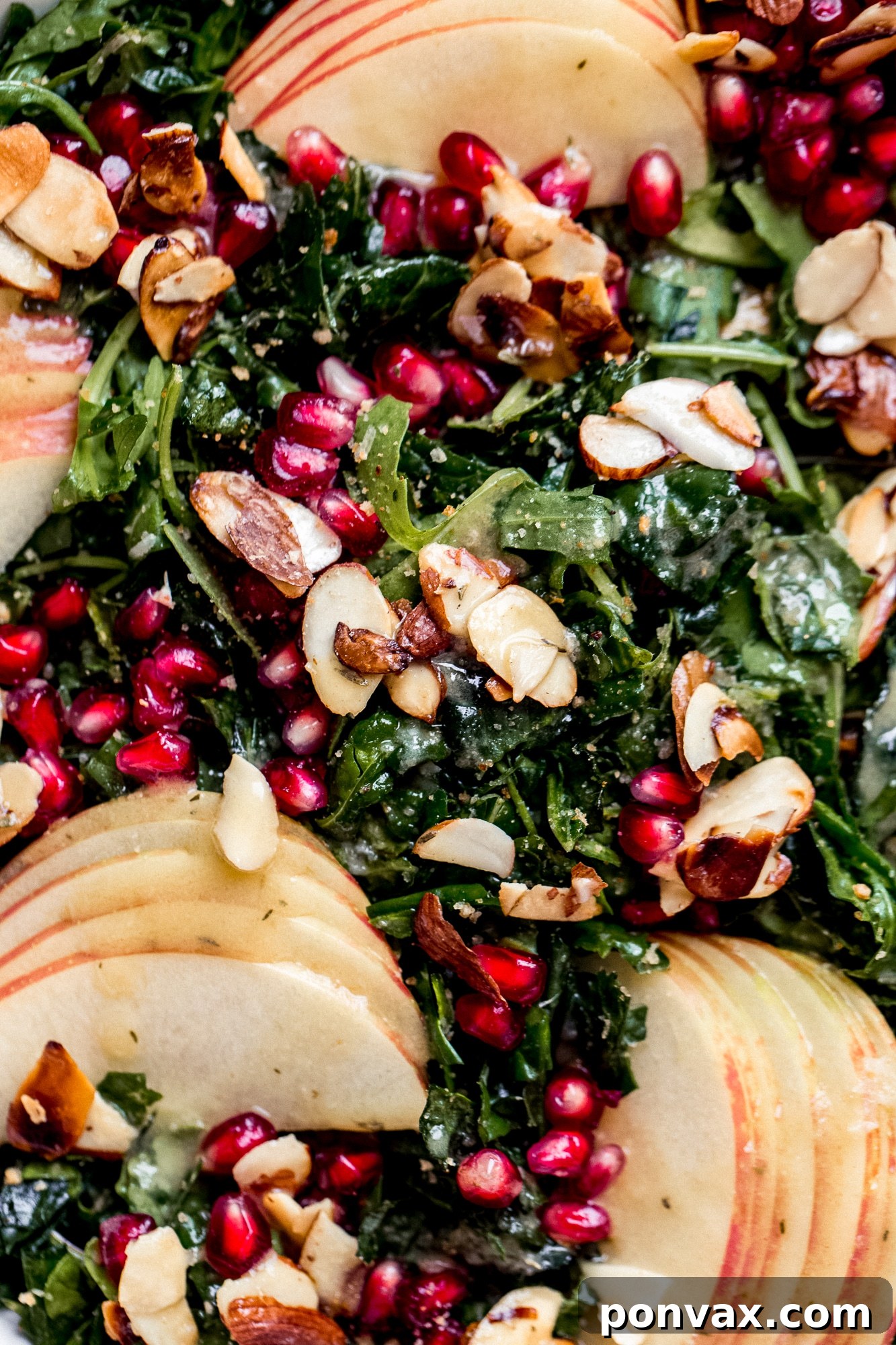 Overhead shot of Autumn Kale Harvest Salad on a white platter, showcasing the beautiful arrangement of fresh kale, ruby red pomegranate seeds, crisp apple slices, and golden candied almonds, ready to be served.