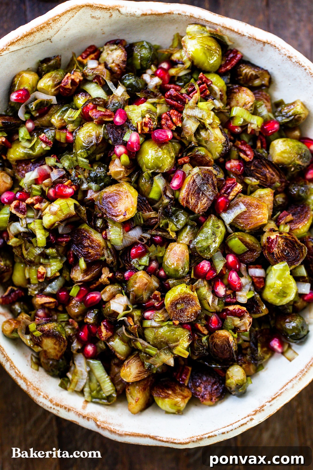 Jewel-Toned Roasted Brussels Sprouts with Pomegranate and Pecans 2 Beautifully roasted Brussels sprouts garnished with vibrant pomegranate seeds and toasted pecans in a serving bowl.