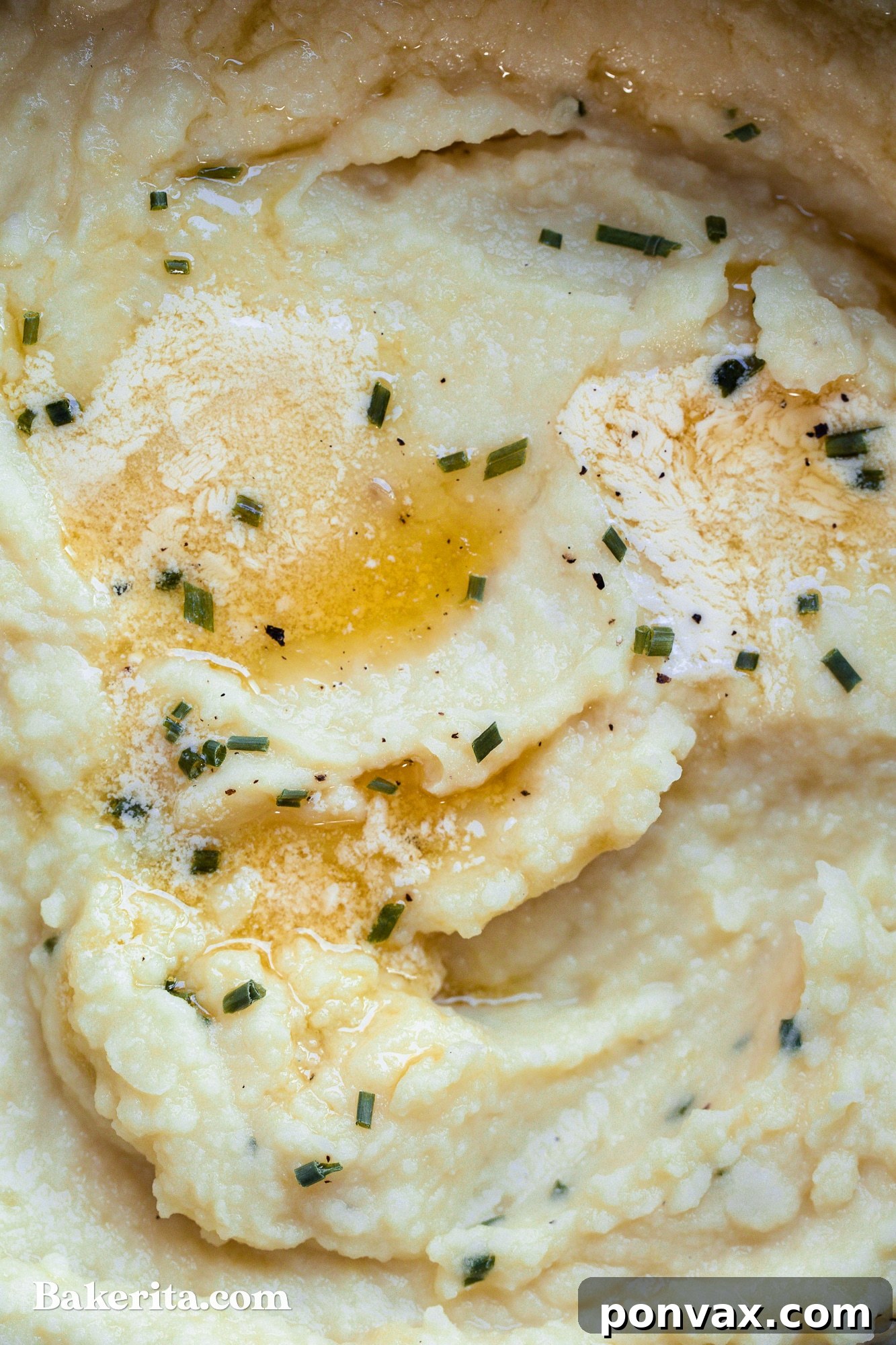 A large serving bowl filled with creamy vegan mashed potatoes, garnished with chives and a drizzle of gravy.