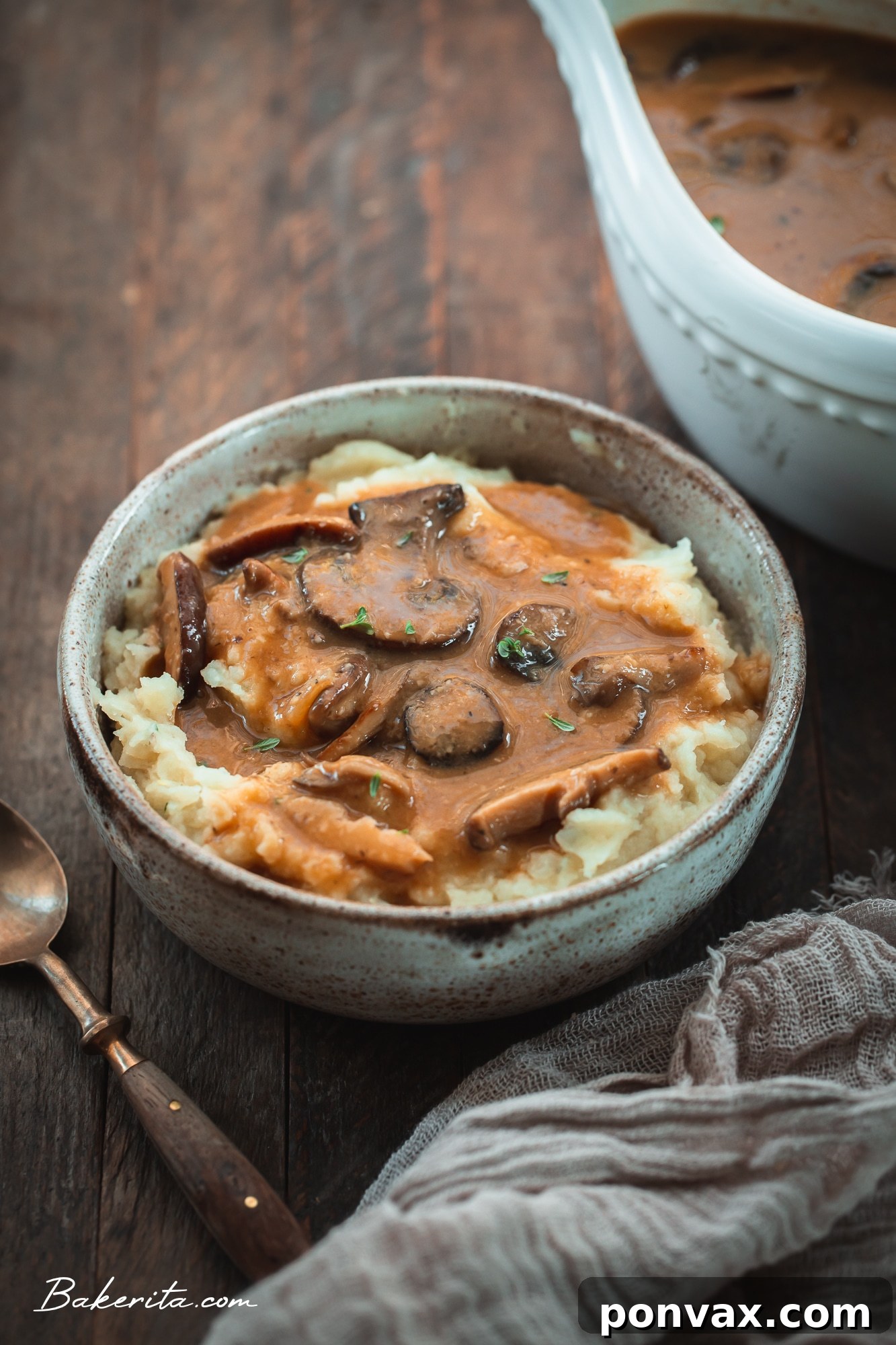 A bowl of mashed potatoes topped with vegan mushroom gravy and fresh herbs.