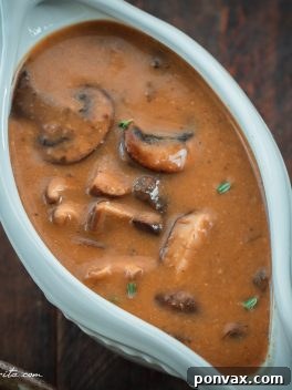 Delicious Vegan Mushroom Gravy in a gravy boat, garnished with fresh herbs.