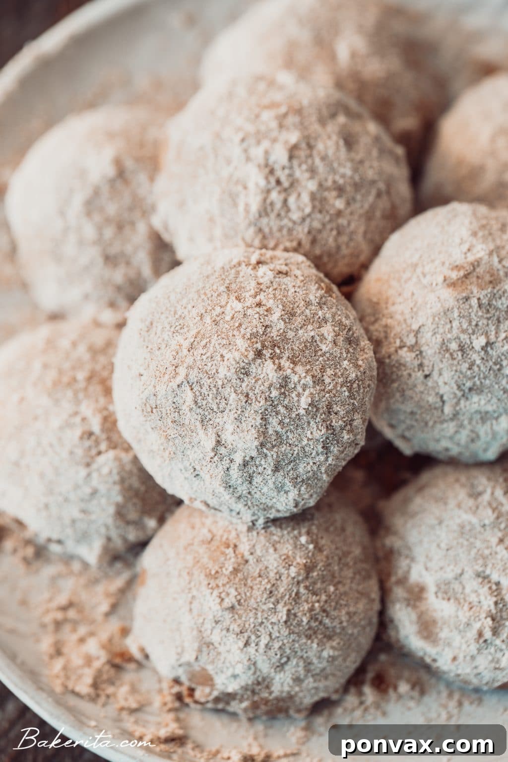 Three snowball cookies on a light-colored cloth, with one broken open to show the pecan pieces inside