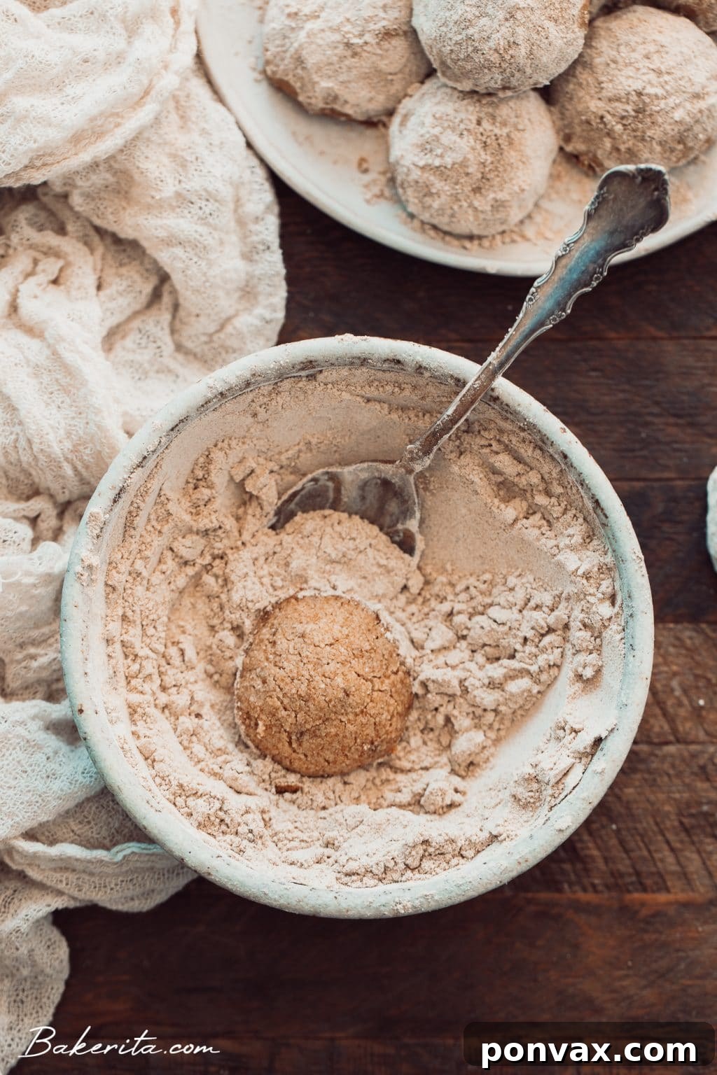 A baking sheet with freshly baked snowball cookies, some already rolled in powdered sugar
