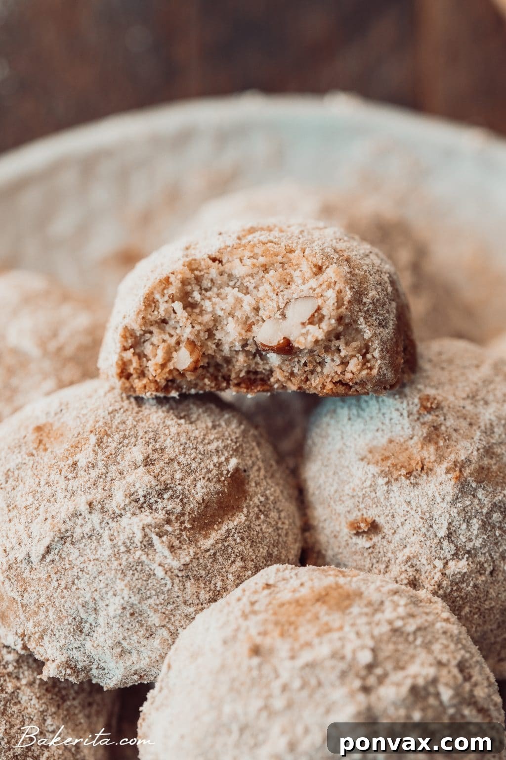A hand holding a snowball cookie, revealing its perfectly round shape and white coating