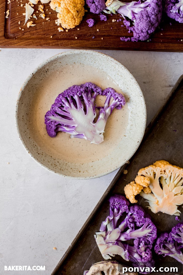 Hand drizzling tahini sauce over cut cauliflower steaks on a baking sheet, ready for roasting.