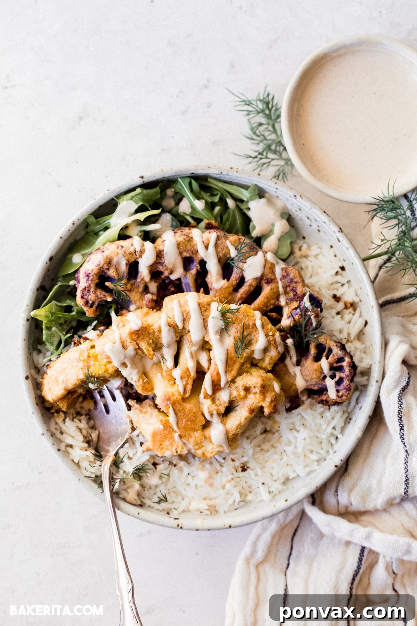 Close-up of a serving of Vegan Tahini Cauliflower Steaks with rice and greens, drizzled with tahini sauce.