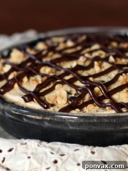 A slice of Chocolate Peanut Butter Mousse Pie with an Oreo crust, creamy peanut butter mousse, chocolate drizzle, and chopped peanuts.