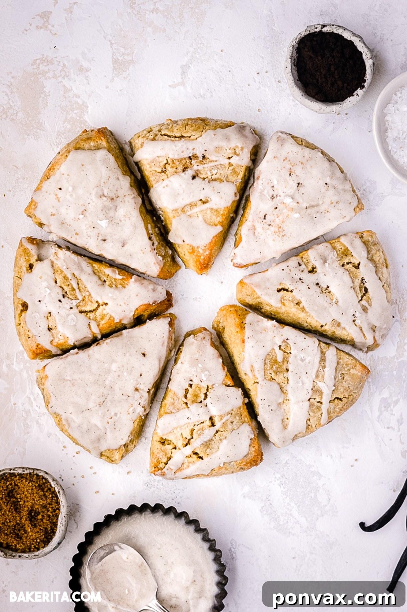 Eight Vanilla Bean Scones arranged in a circle, topped with vanilla bean glaze. Vanilla bean powder in a bowl on the top right, with vanilla bean placed on the bottom left.
