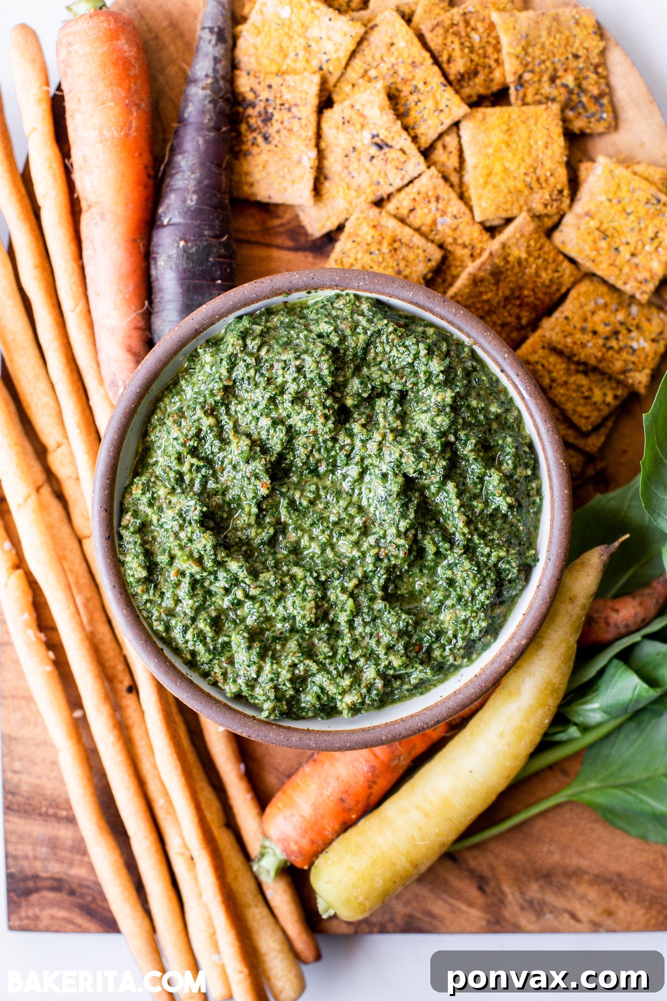 Zero-Waste Vegan Carrot Green Pesto 2 Vibrant green carrot top pesto in a glass jar, garnished with a fresh sprig of basil and a lemon slice, on a rustic wooden board.