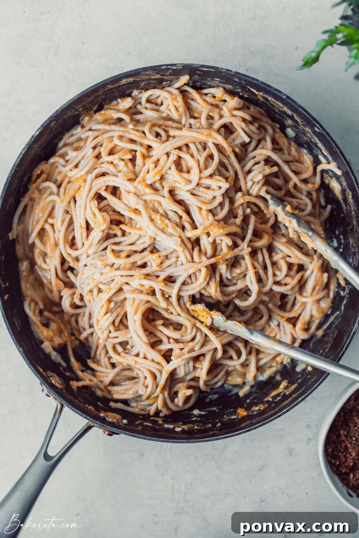 A close-up shot of a single serving of one-pot creamy lemon pasta in a white bowl, garnished with fresh herbs.