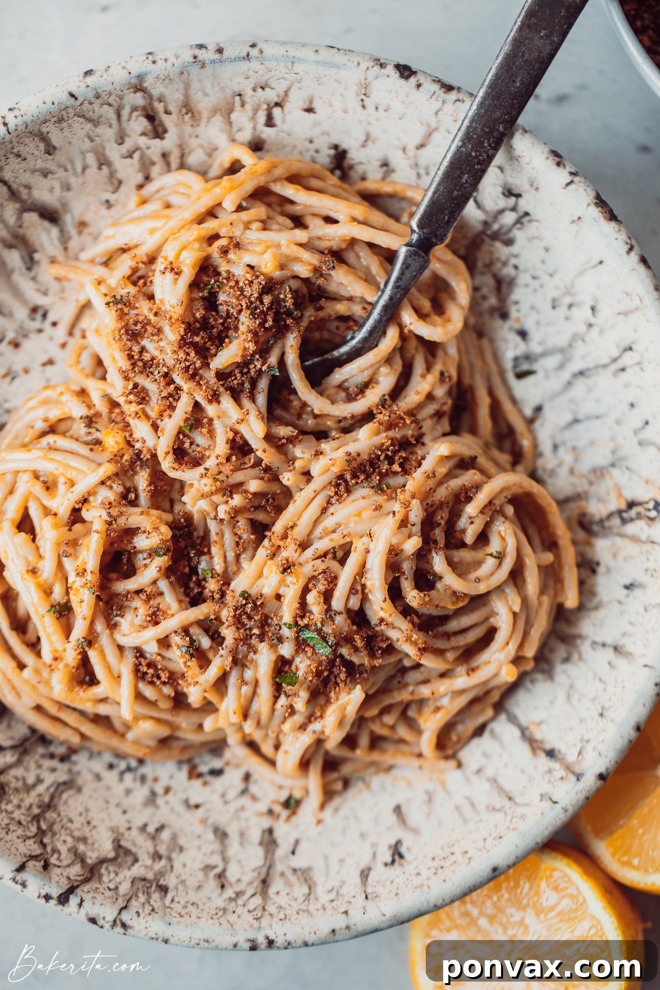 A hand stirring the creamy lemon pasta in a pan, with a wooden spoon, showcasing its rich texture.