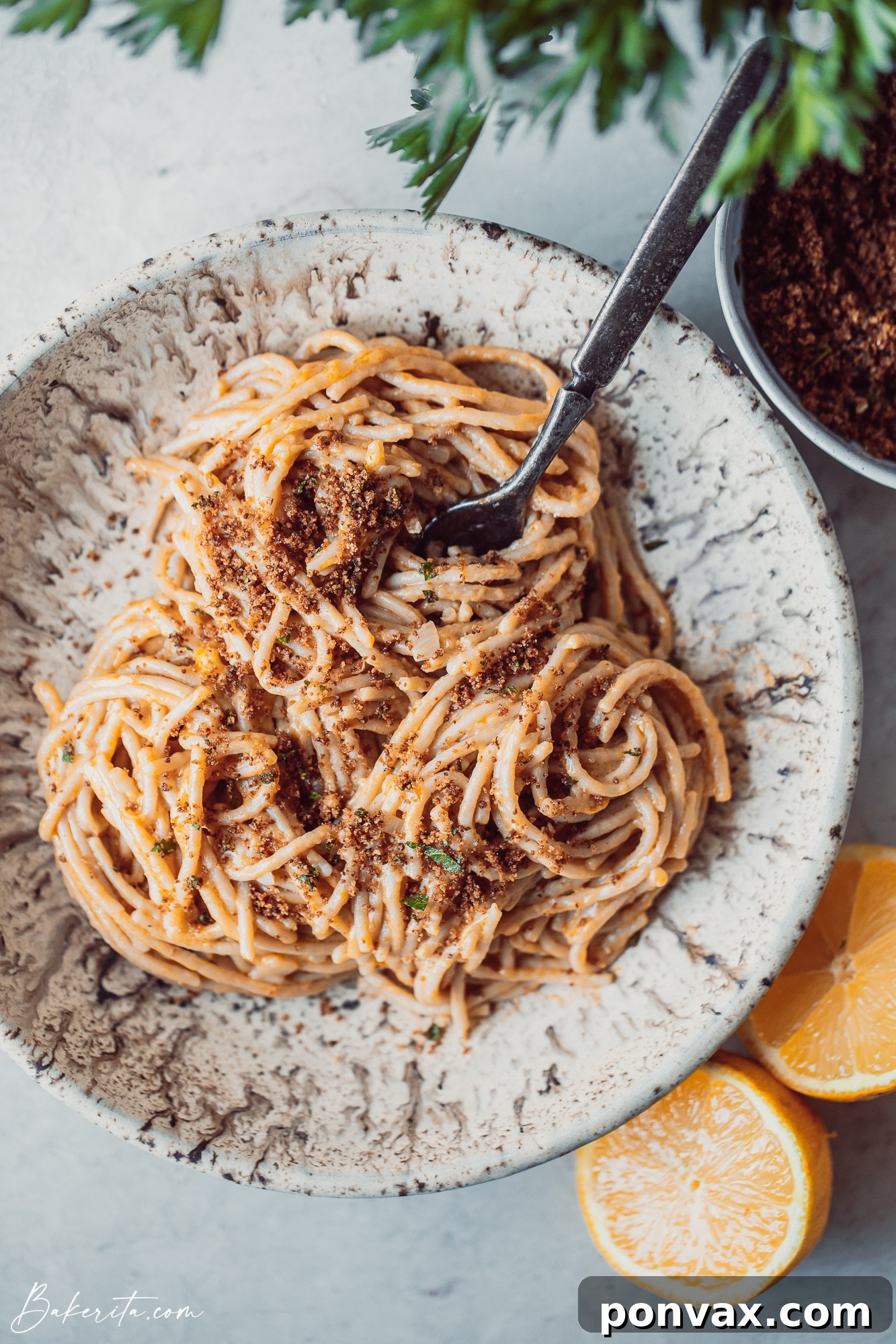 A bowl of creamy lemon pasta topped with fresh greens and what appears to be toasted breadcrumbs, ready to eat.