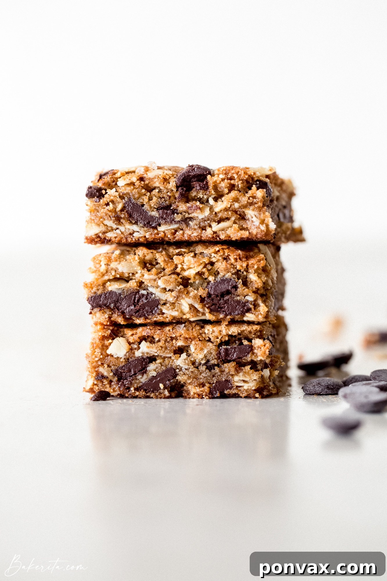 Decadent Plant-Based Oat Chocolate Squares 6 A stack of three Vegan Gluten-Free Oatmeal Chocolate Chip Bars with a bite taken out of the top one, revealing the soft, chewy interior.