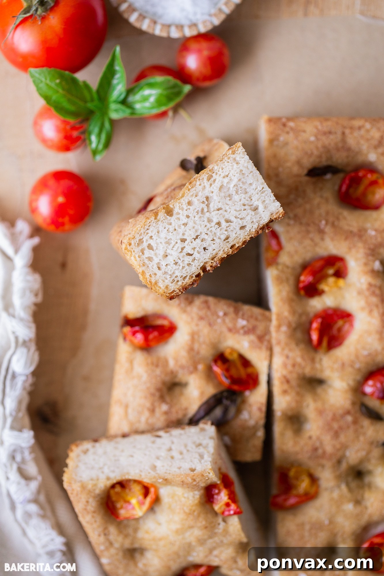 Freshly baked gluten-free sourdough focaccia bread, topped with cherry tomatoes and herbs, resting on a wooden board.