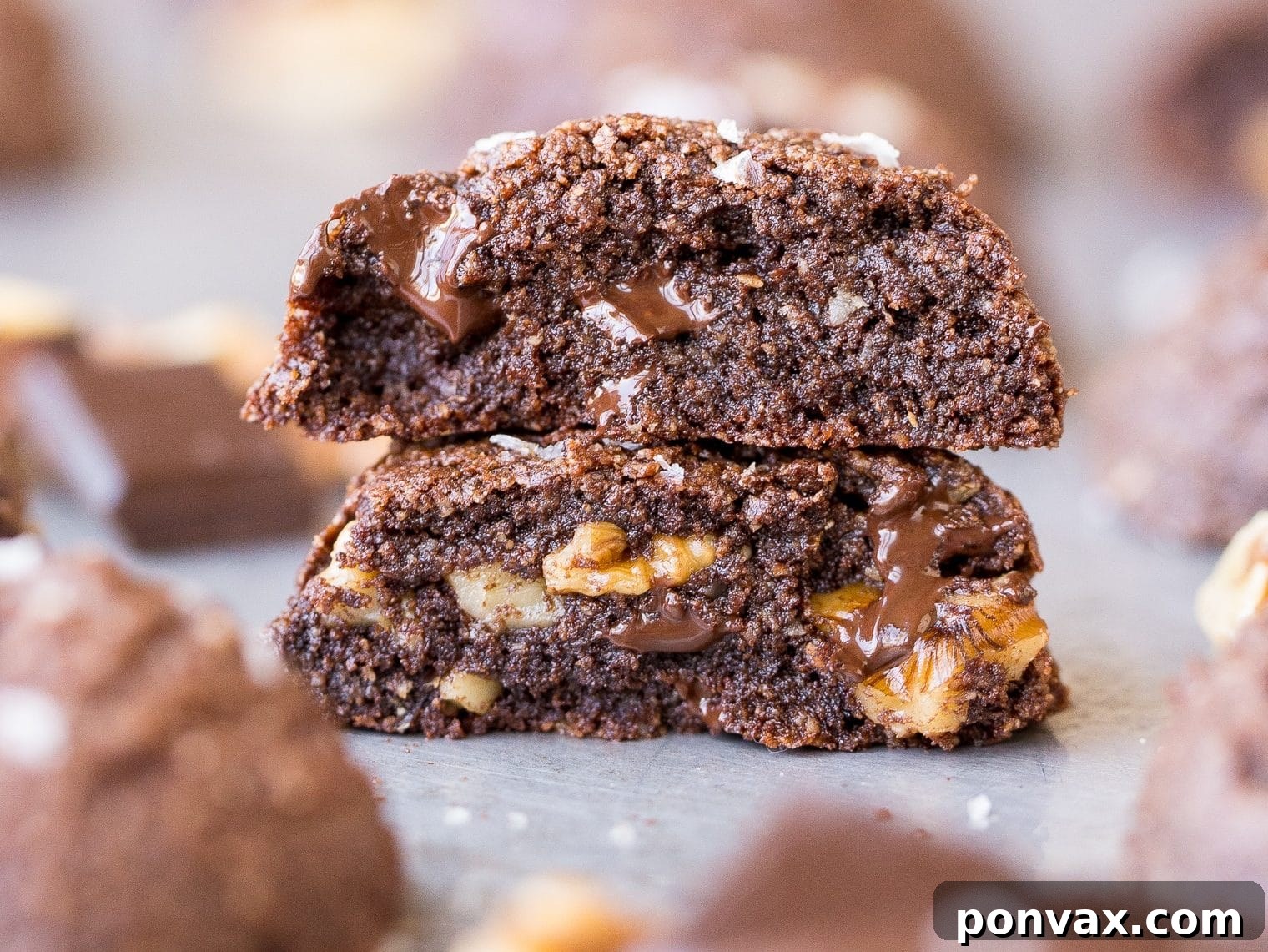 25+ Delicious Vegan Cookie Recipes 26 A close-up shot of a rich, dark chocolate chunk cookie with visible melty chocolate and walnuts, placed on a white surface.