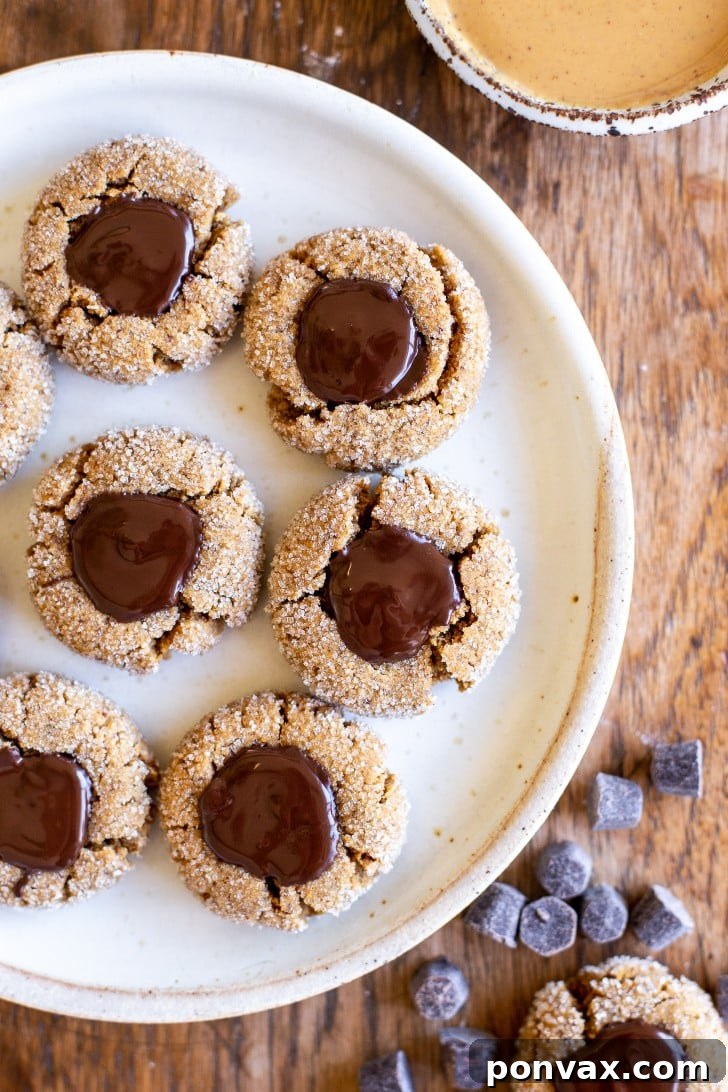 25+ Delicious Vegan Cookie Recipes 4 Three beautifully presented gluten-free peanut butter blossom cookies with dark chocolate centers, sitting on a wooden cutting board with scattered peanuts, evoking a sense of healthy indulgence.